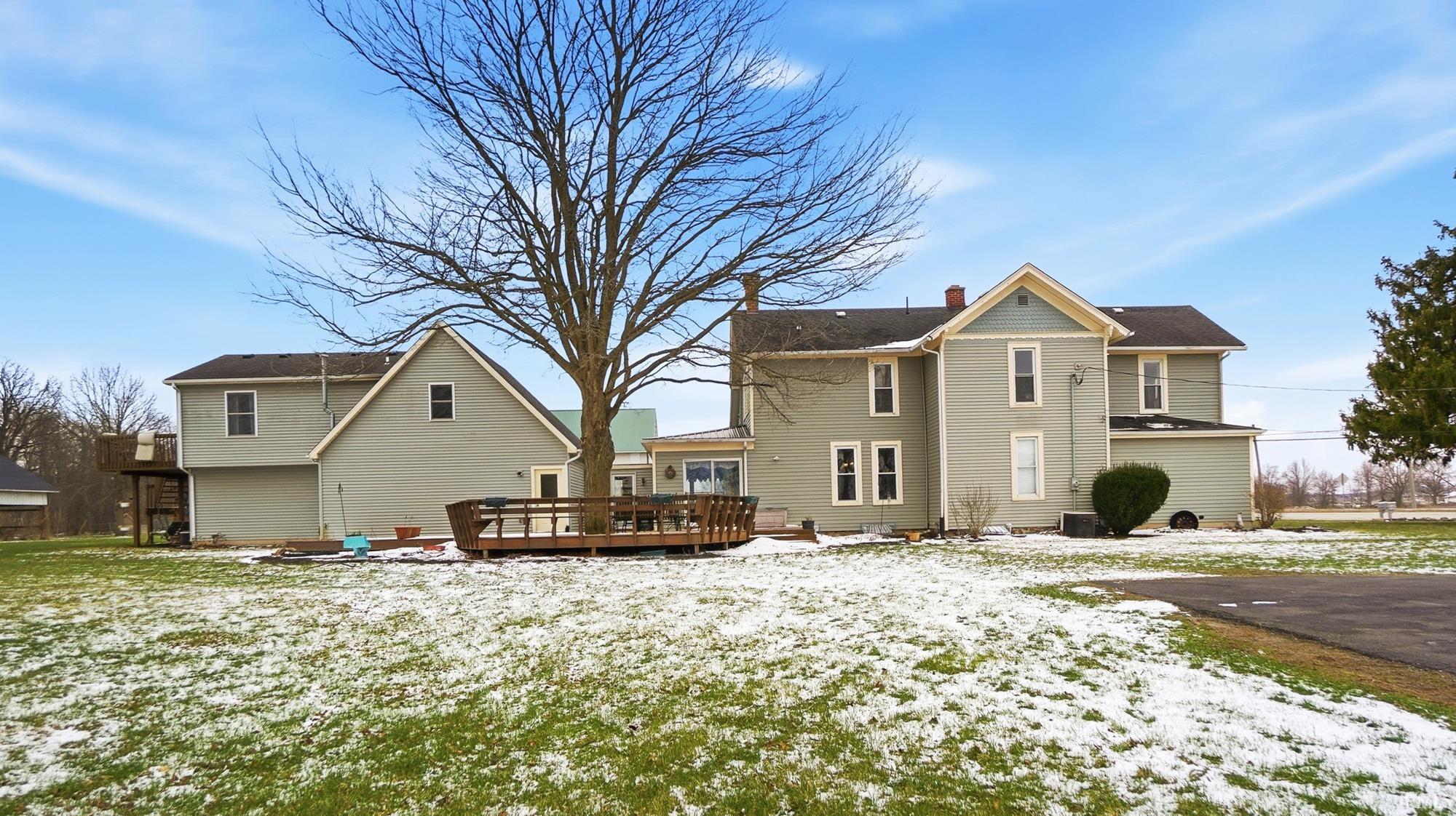 Snow covered back of property with a deck and a chimney