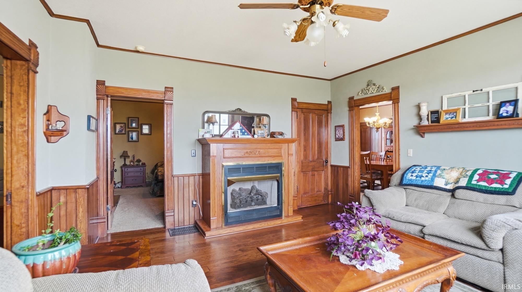 Living area featuring wooden walls, hardwood / wood-style floors, a fireplace with raised hearth, a wainscoted wall, and ornamental molding