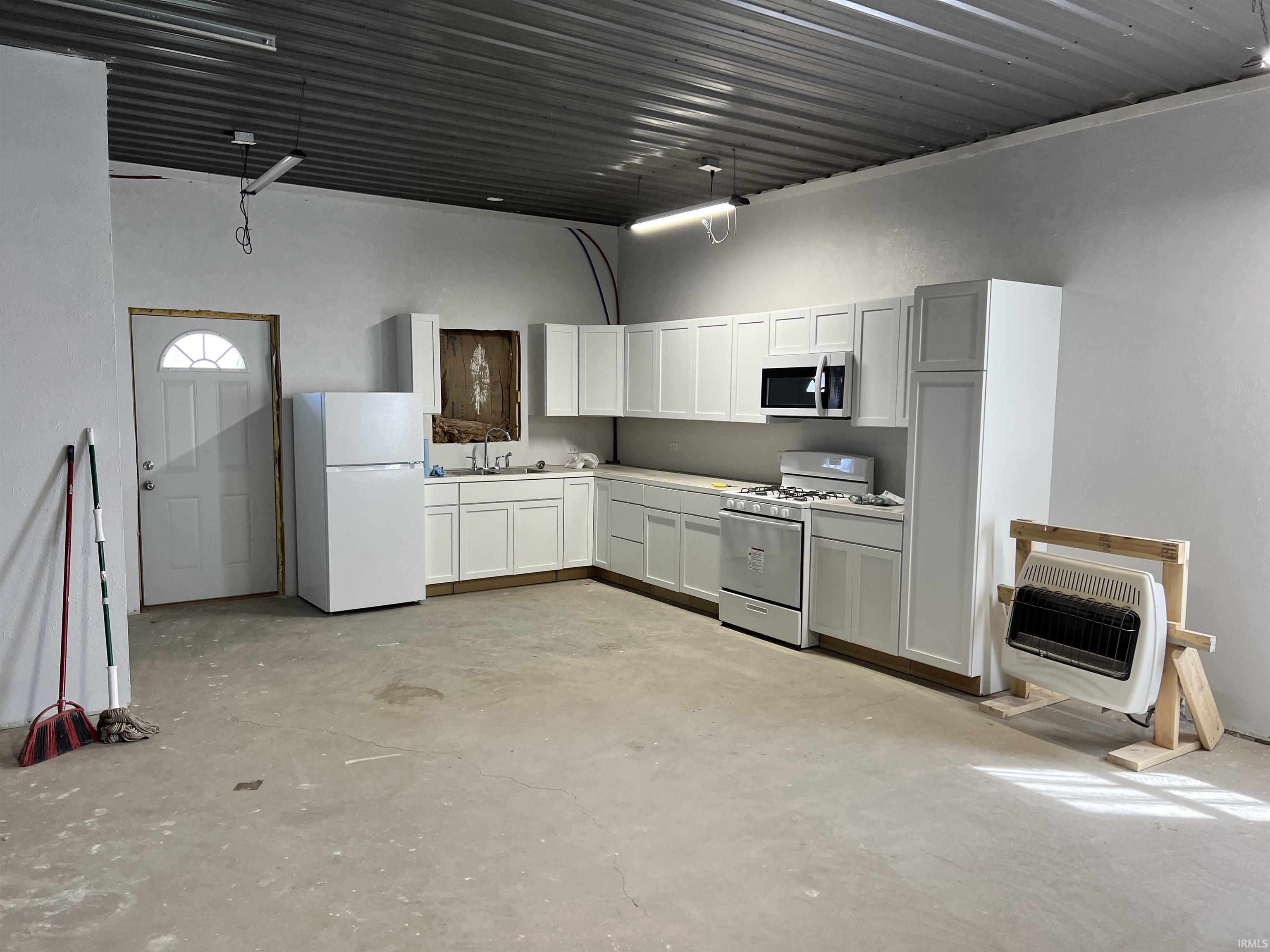 Kitchen featuring unfinished concrete flooring, white appliances, heating unit, and light countertops