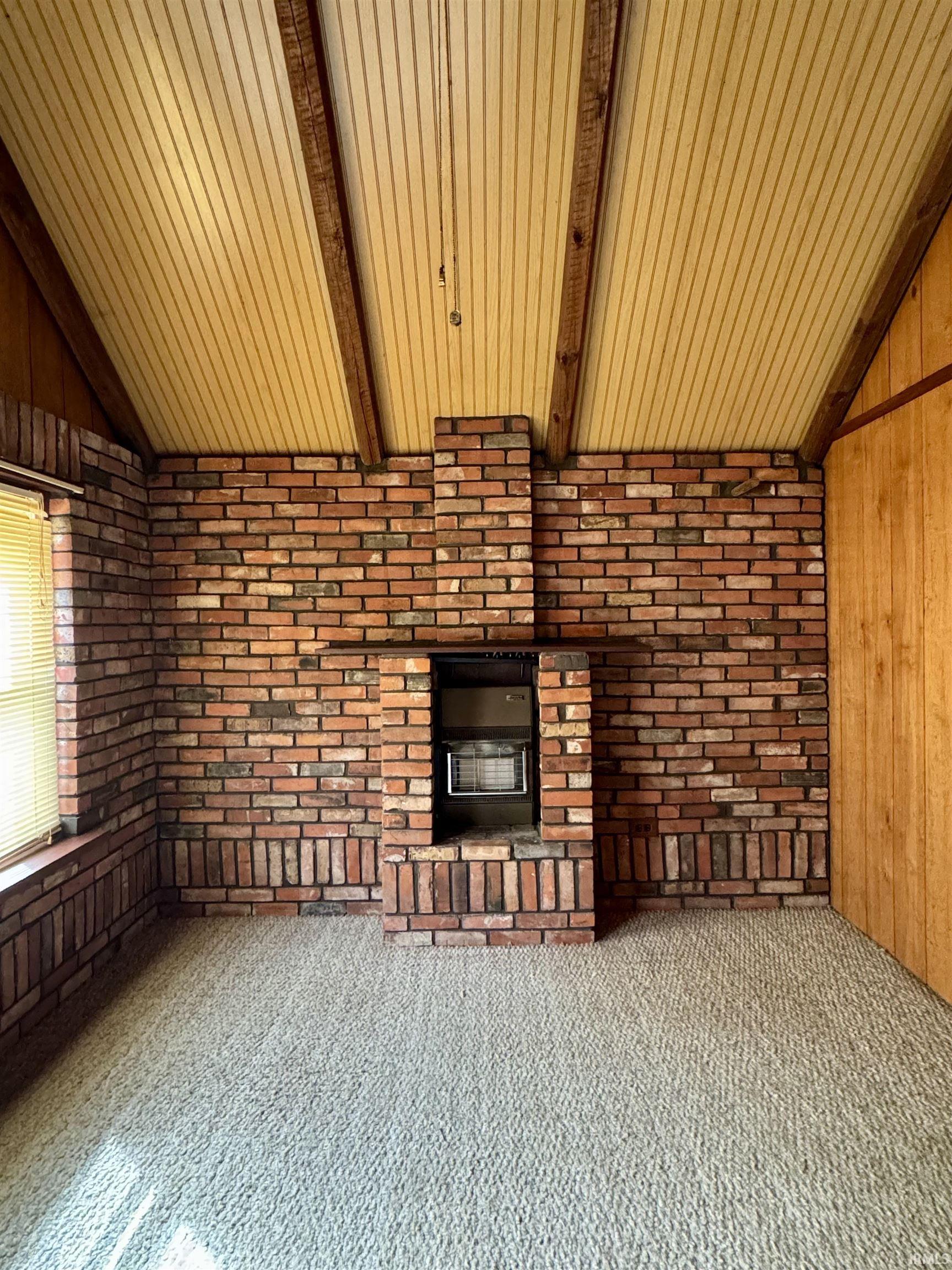 Unfurnished living room with vaulted ceiling with beams, brick wall, wood walls, and carpet floors