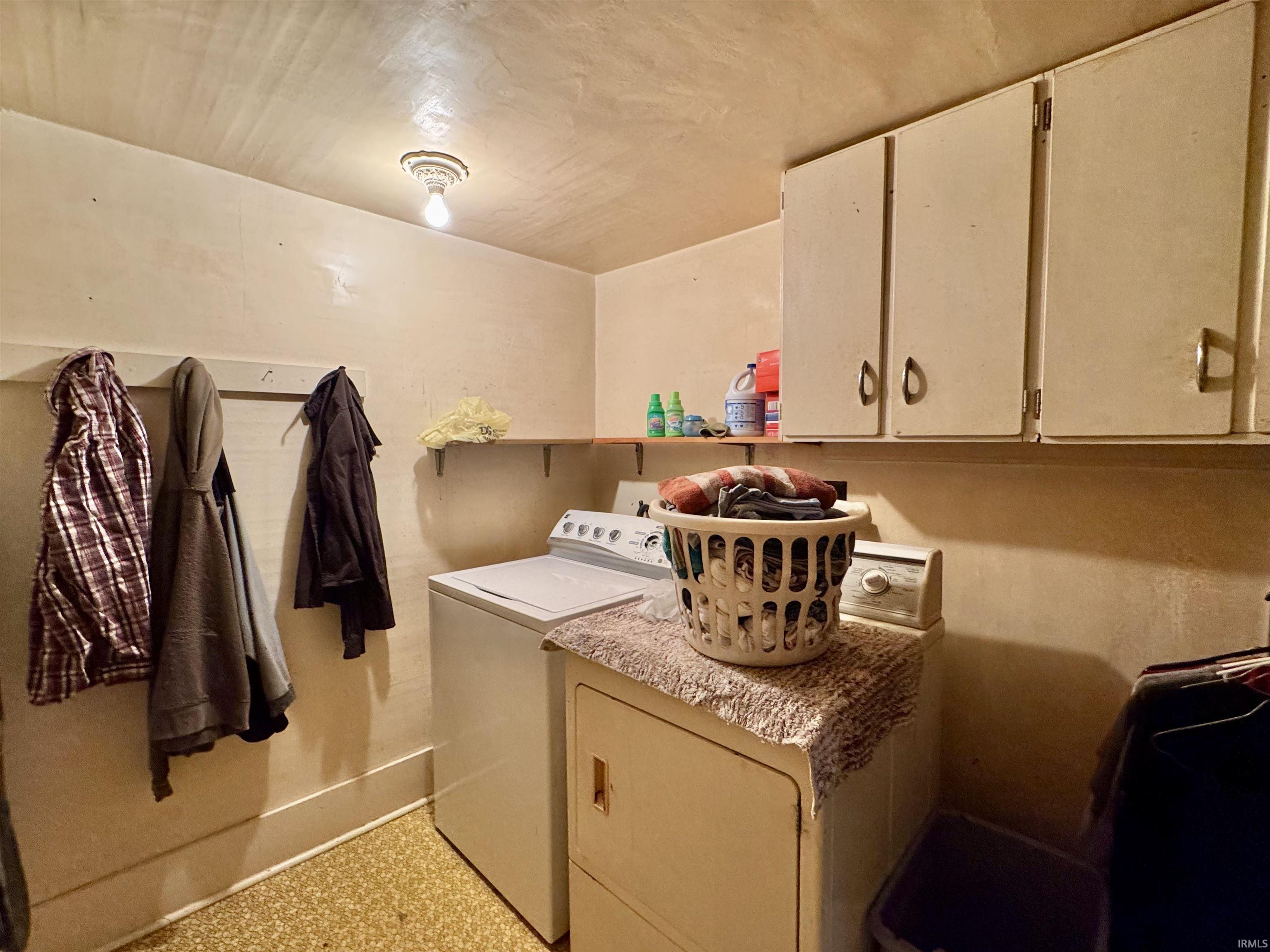Laundry room with washer and dryer, cabinet space, and dark aggregate flooring