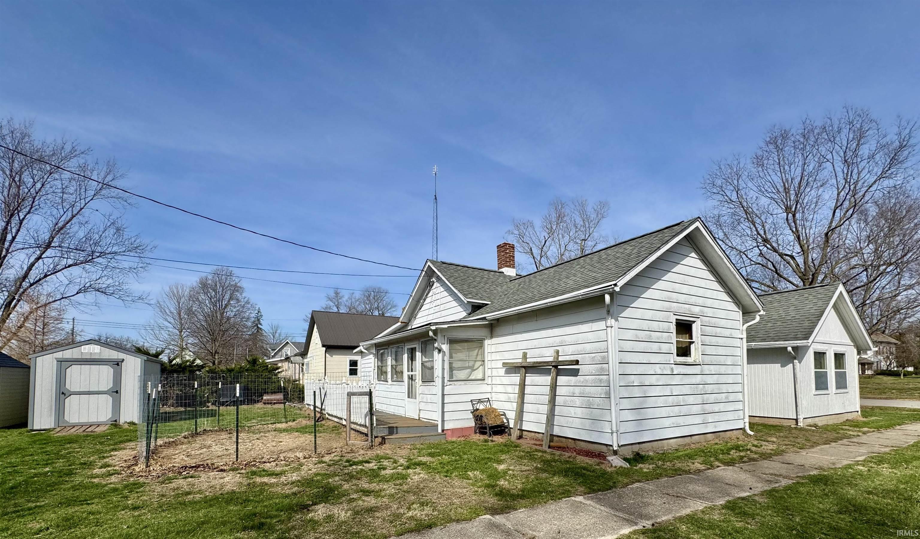 View of side of home featuring roof with shingles, a chimney, and a storage unit