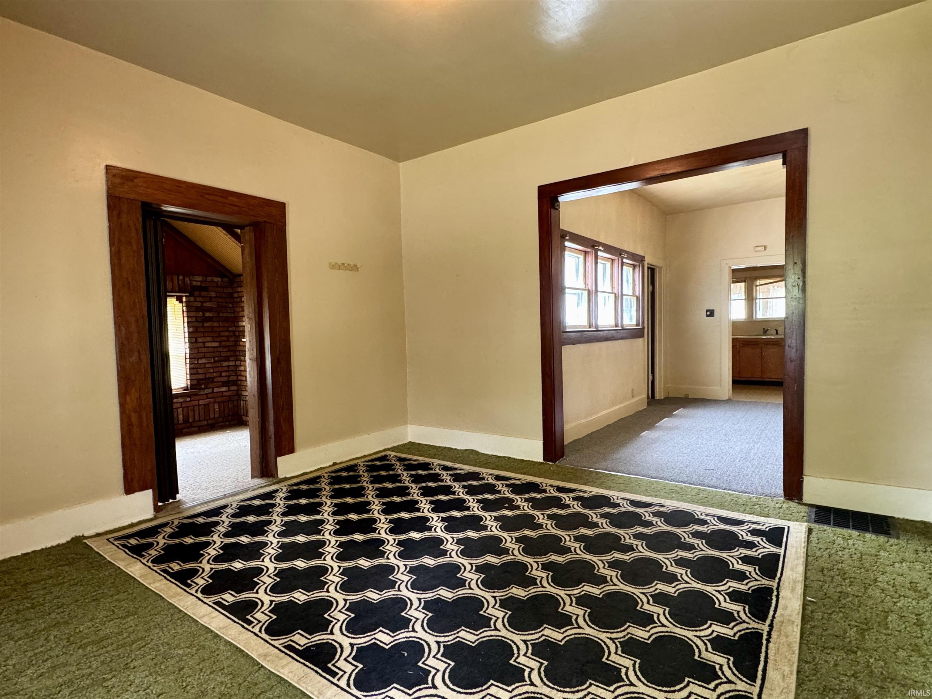 Interior space featuring distinct architectural archways with wood trim, light beige wall paint, and green carpeting