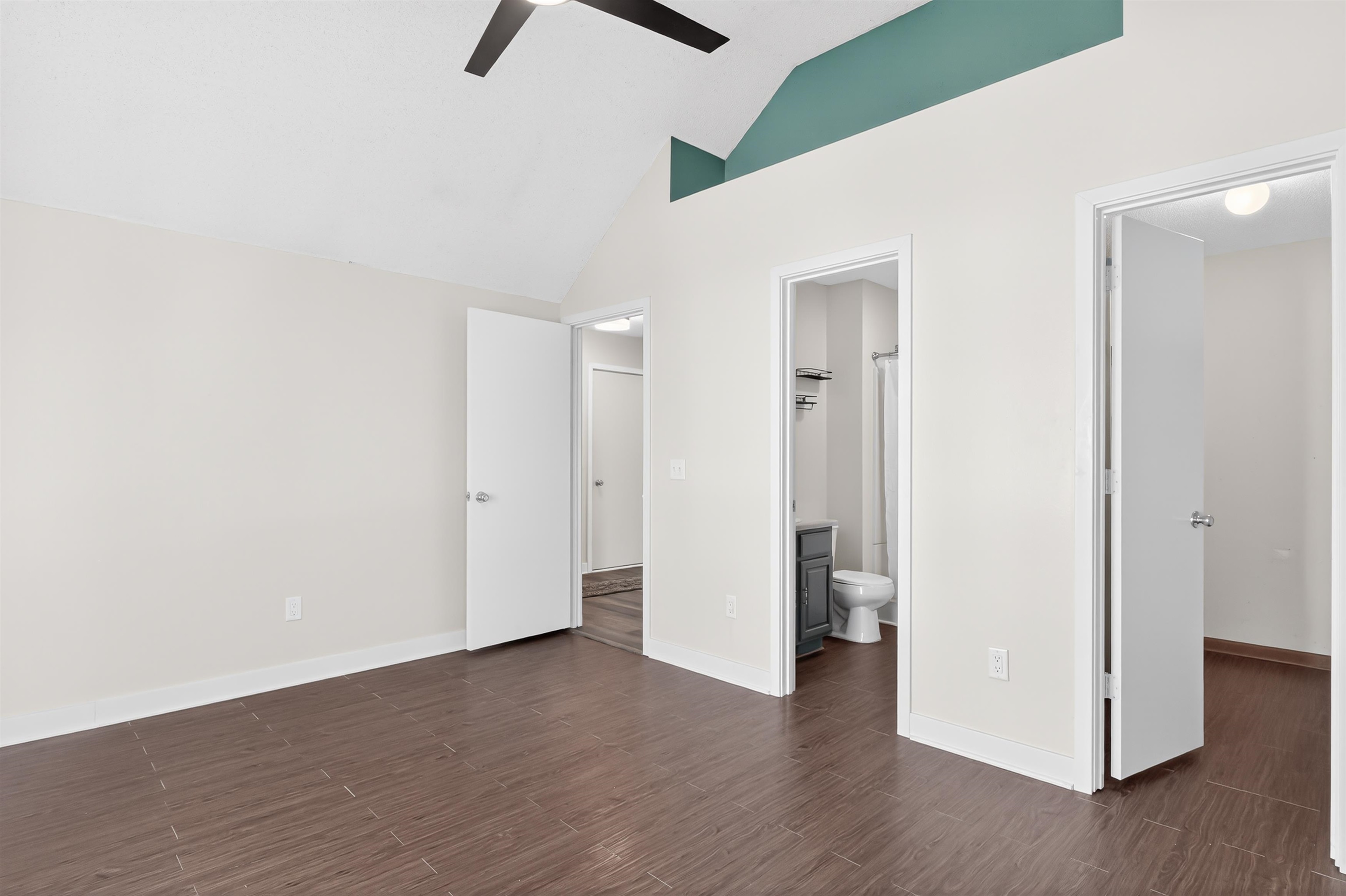 Unfurnished bedroom with vaulted ceiling, dark wood-type flooring, ceiling fan, and ensuite bathroom