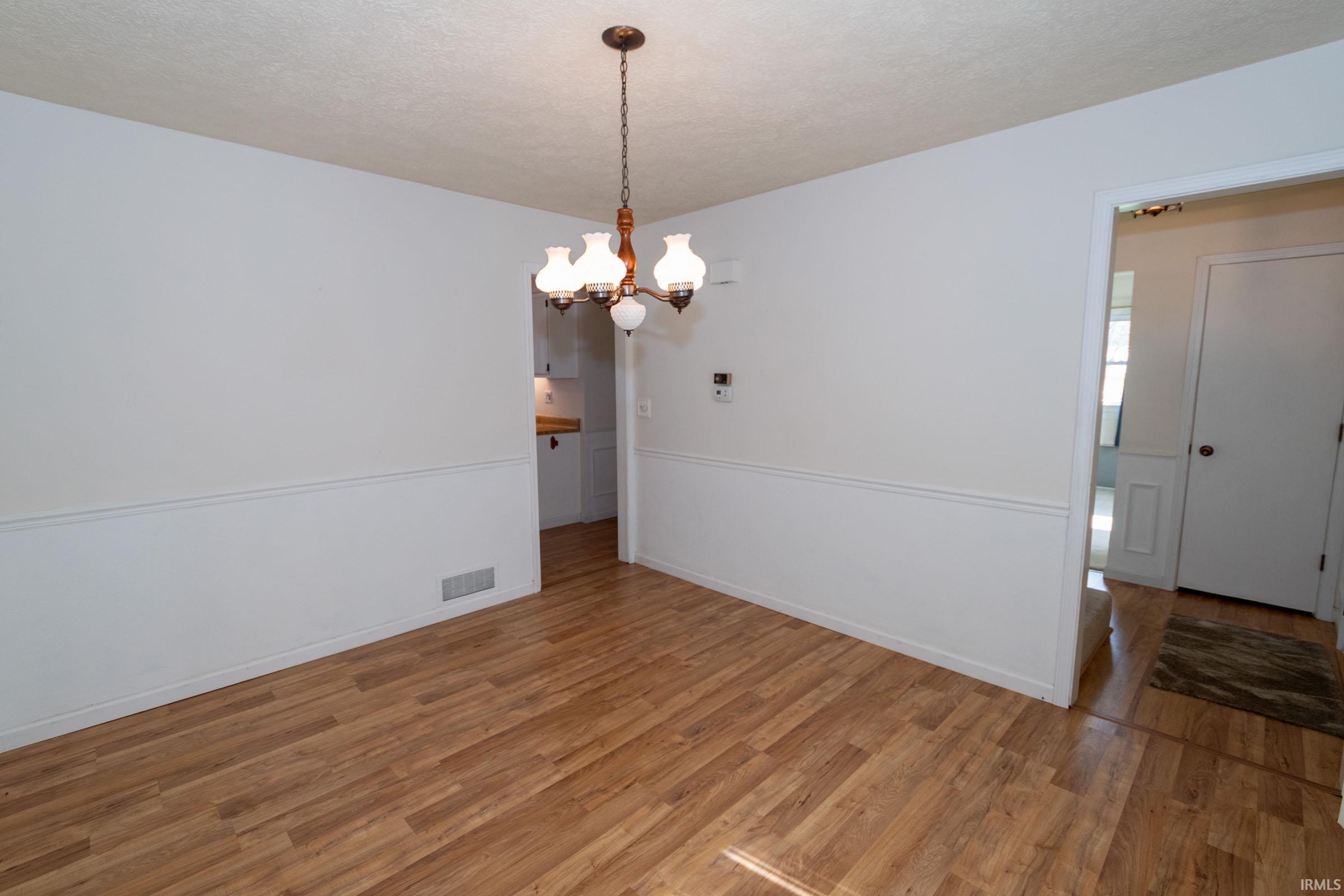 Unfurnished room featuring suspended lighting, wood finished floors, and a textured ceiling