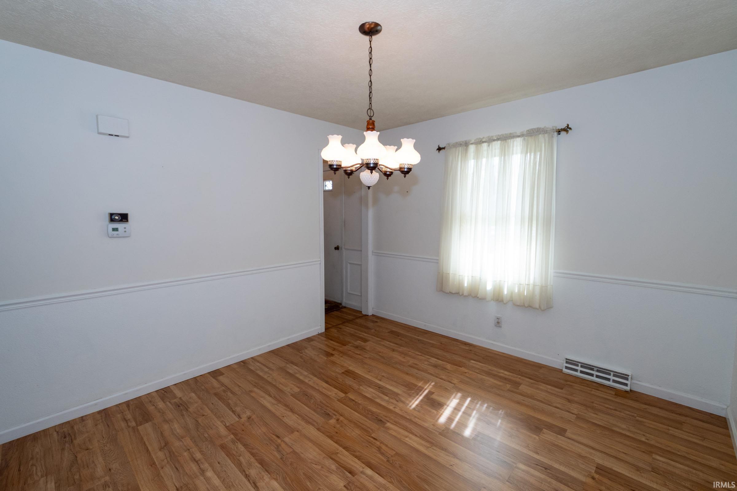 Unfurnished room featuring suspended lighting and wood finished floors