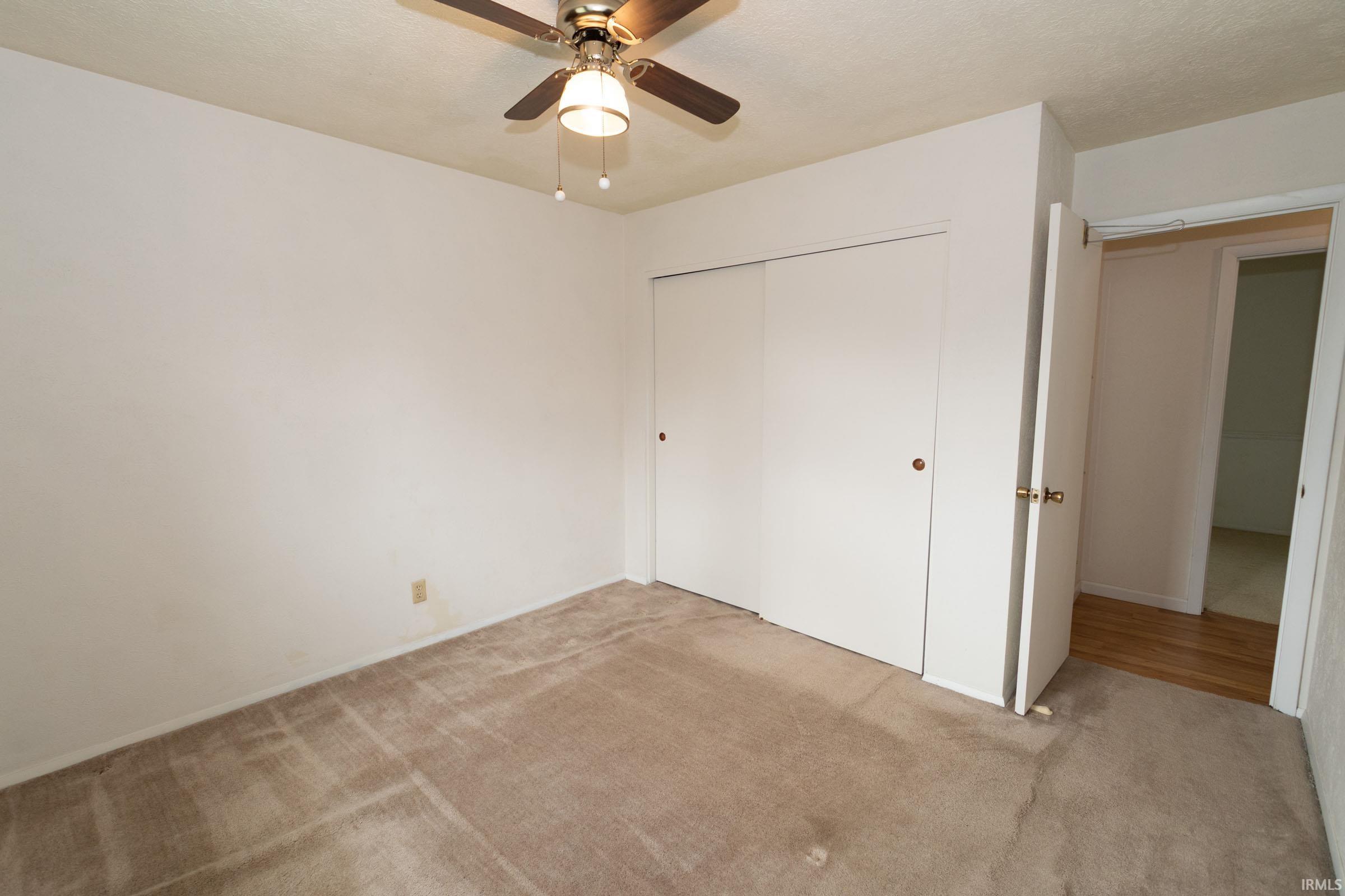 Unfurnished bedroom featuring light colored carpet, a closet, and a ceiling fan