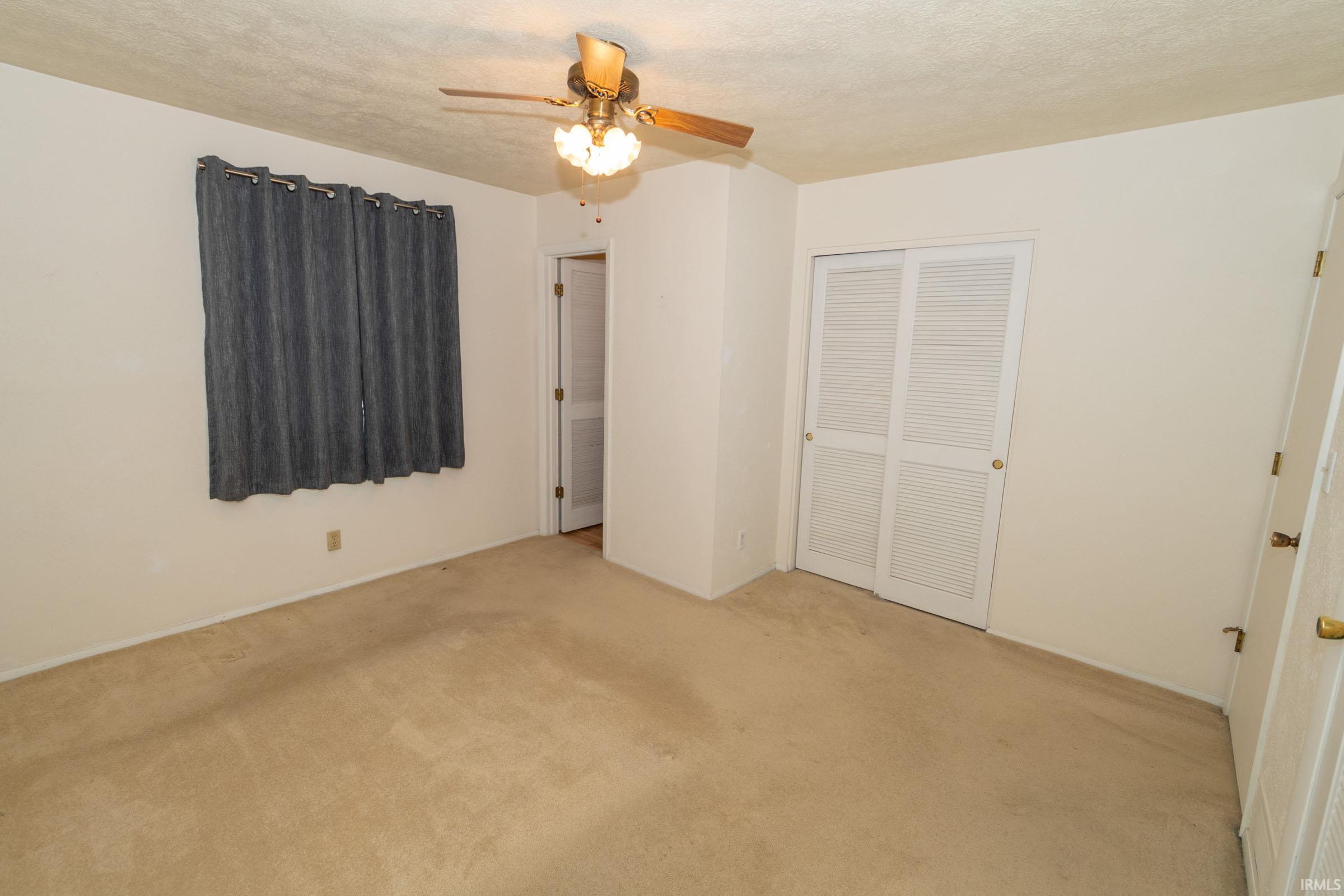Unfurnished bedroom with ceiling fan, light carpet, a closet, and a textured ceiling