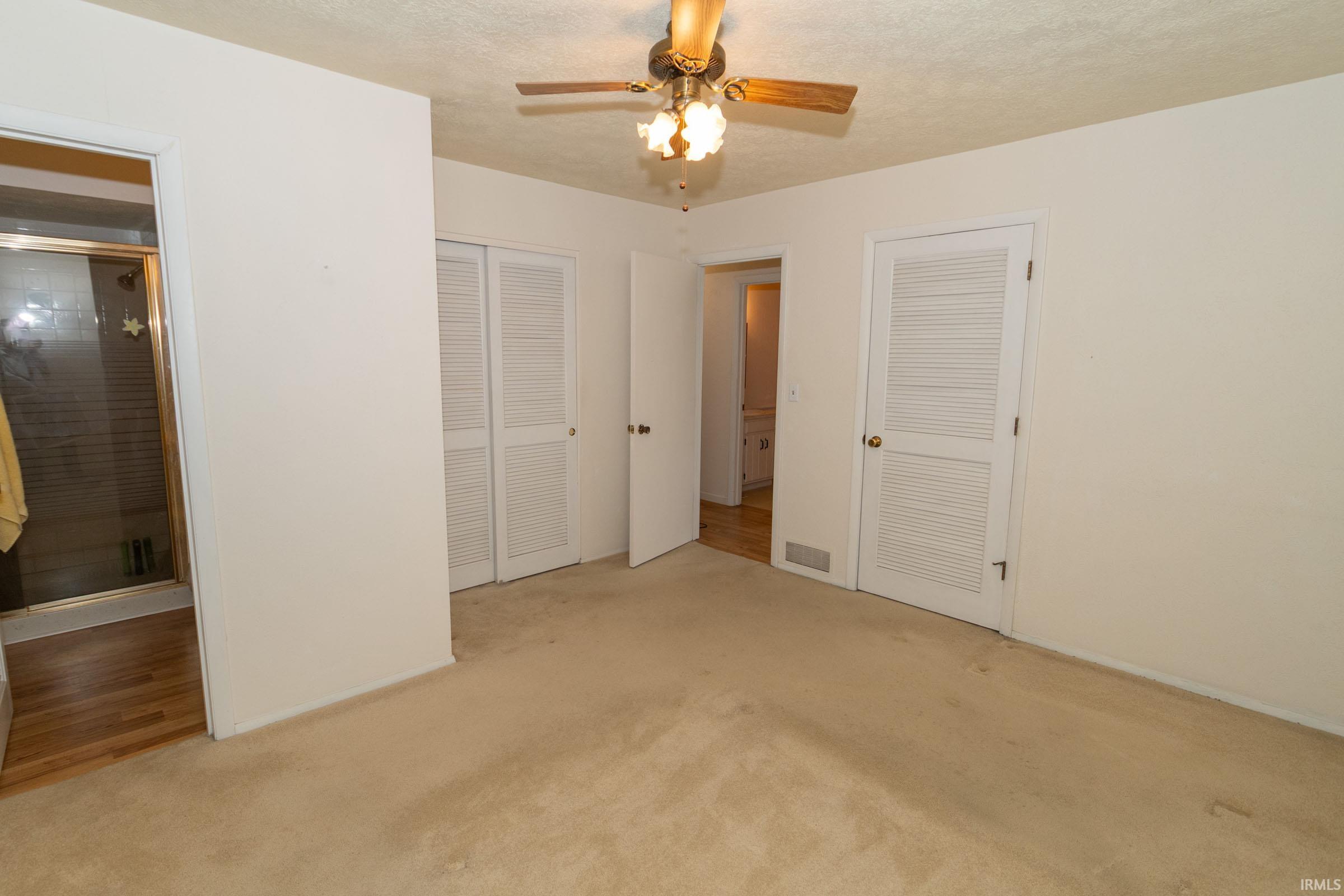 Unfurnished bedroom with two closets, light carpet, ceiling fan, and a textured ceiling