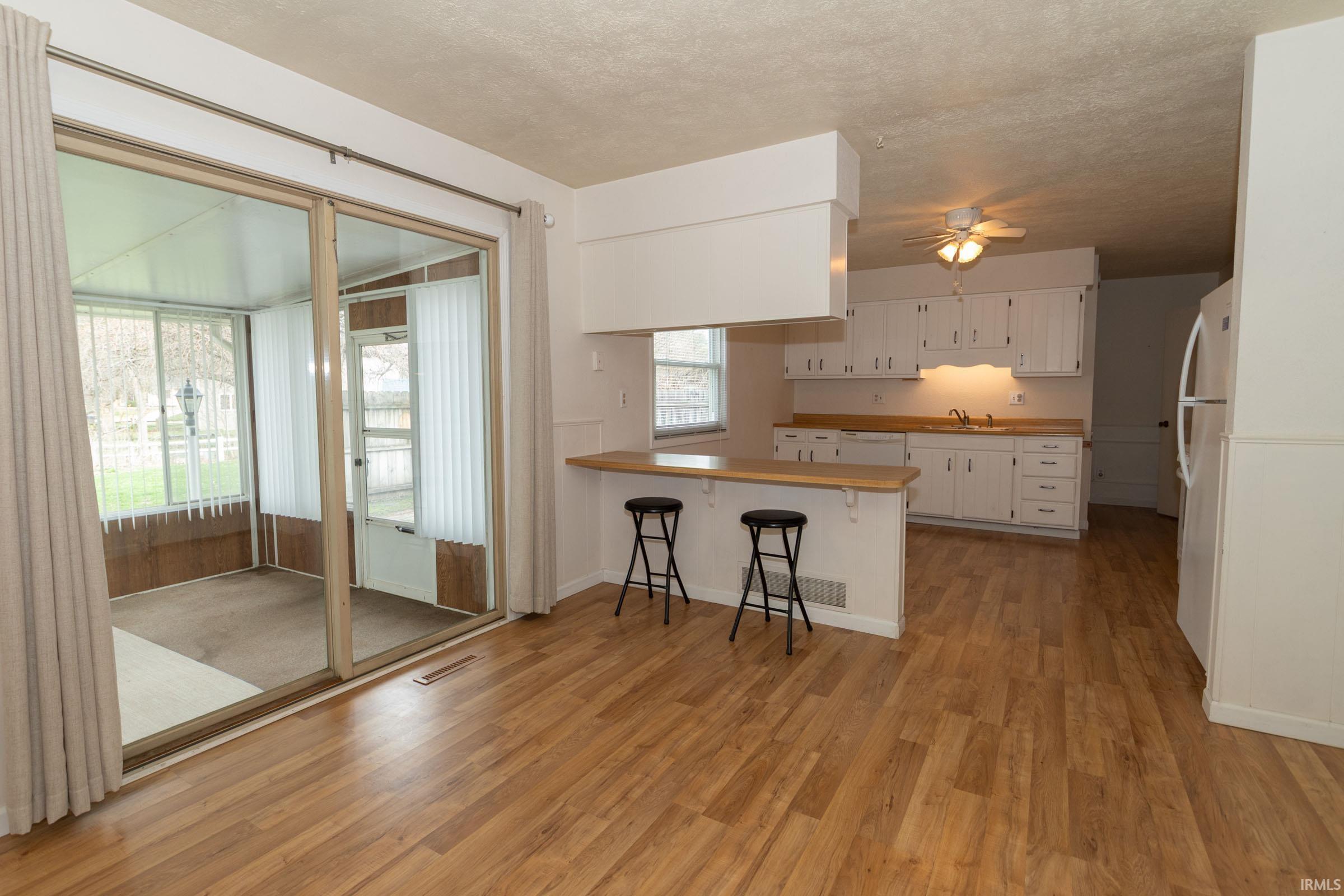 Kitchen with a breakfast bar area, ceiling fan, a peninsula, white appliances, and light wood-type flooring