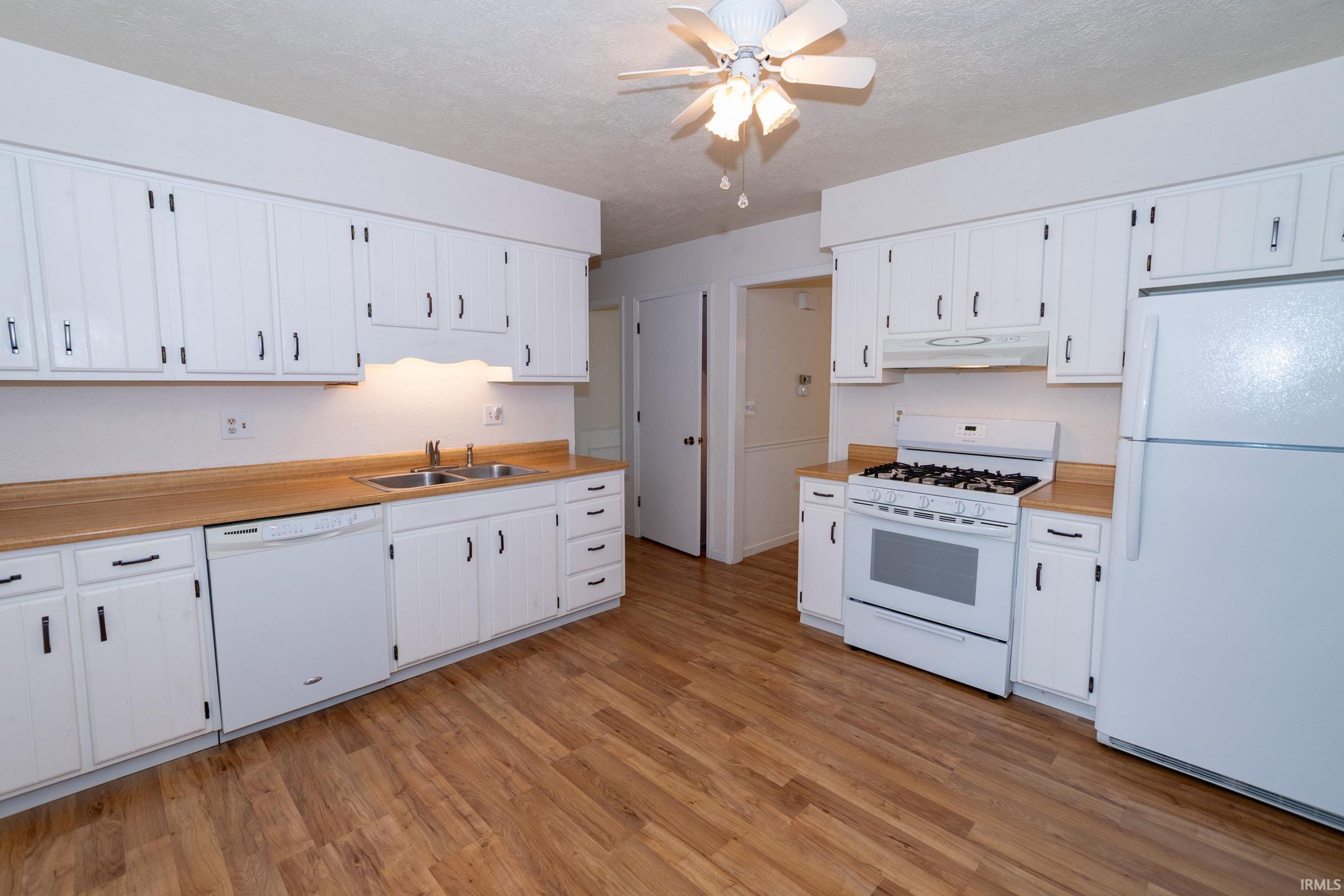 Kitchen featuring white appliances, light countertops, a ceiling fan, light wood-style floors, and white cabinetry