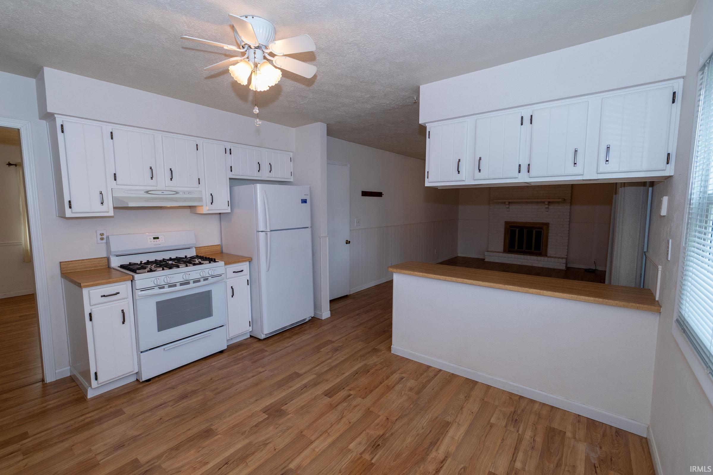 Kitchen with white appliances, white cabinets, a ceiling fan, and a textured ceiling