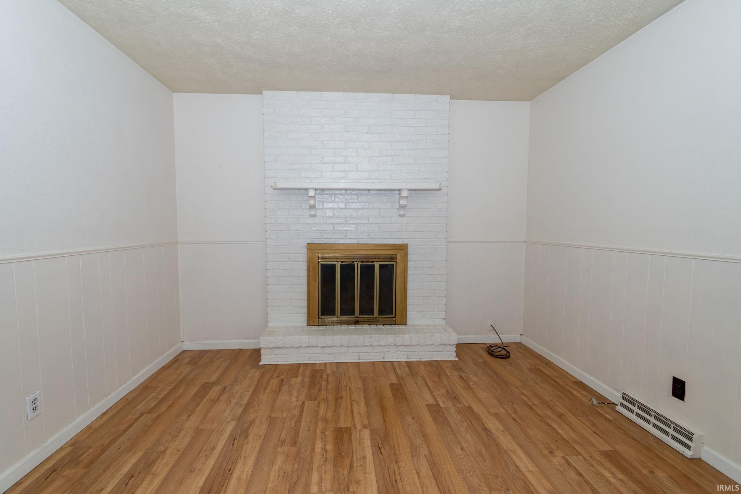 Unfurnished living room with wainscoting, wood finished floors, a textured ceiling, a brick fireplace, and wood walls
