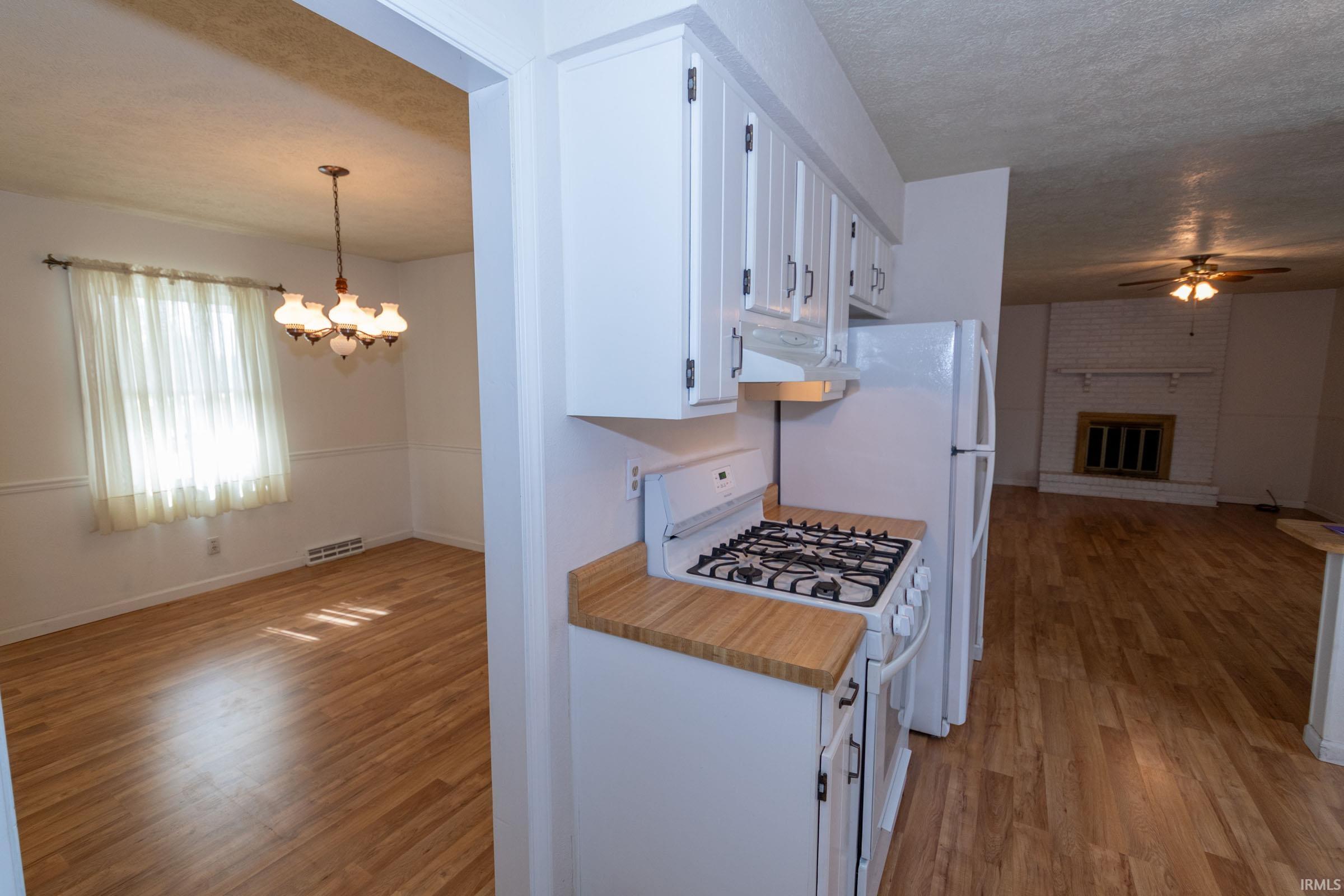 Kitchen with white appliances, white cabinets, light countertops, open floor plan, and a fireplace