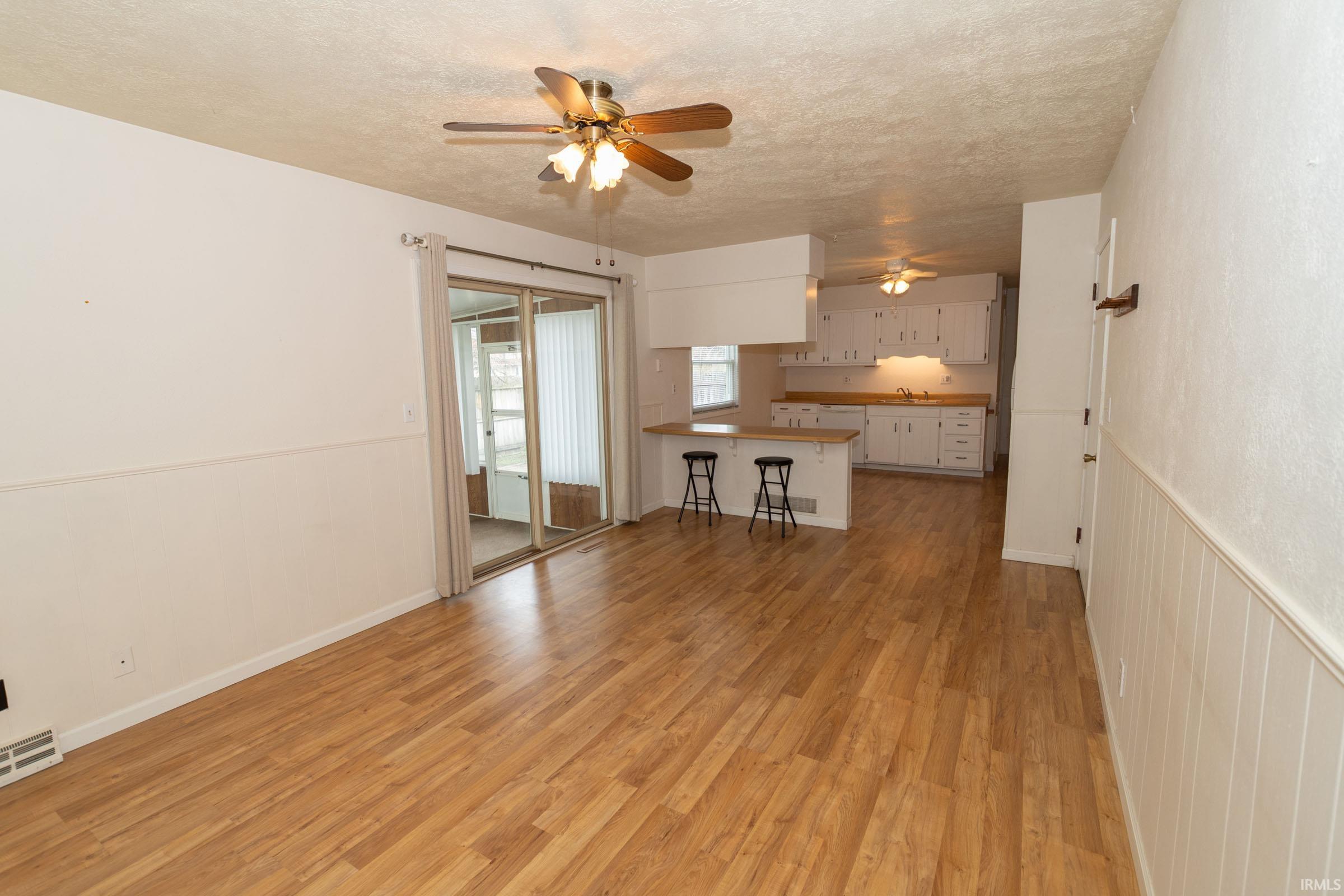 Unfurnished living room featuring ceiling fan, light wood-style flooring, a textured ceiling, and a wainscoted wall
