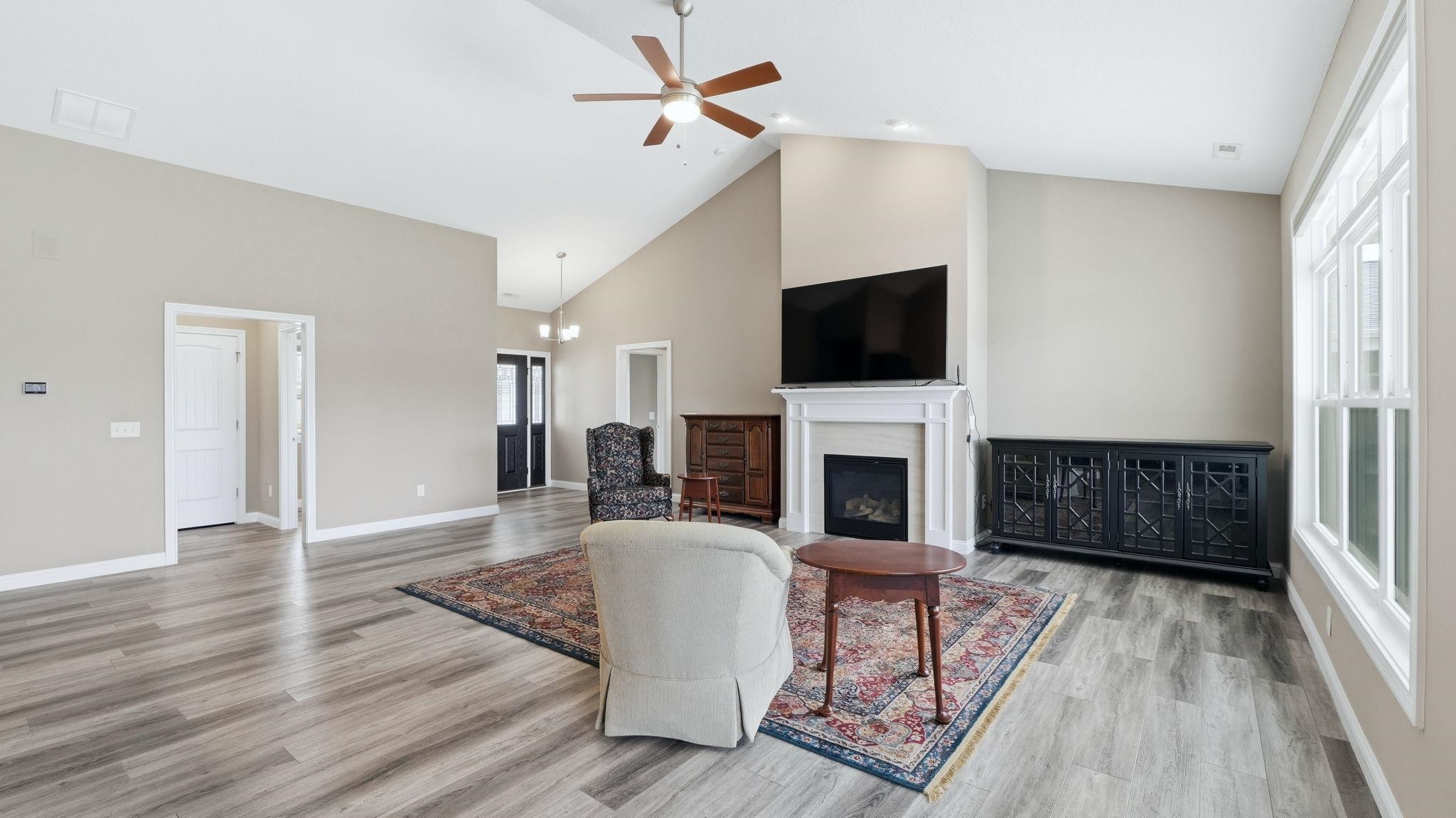 Living room featuring a high ceiling, a ceiling fan, light wood-type flooring, and a glass covered fireplace