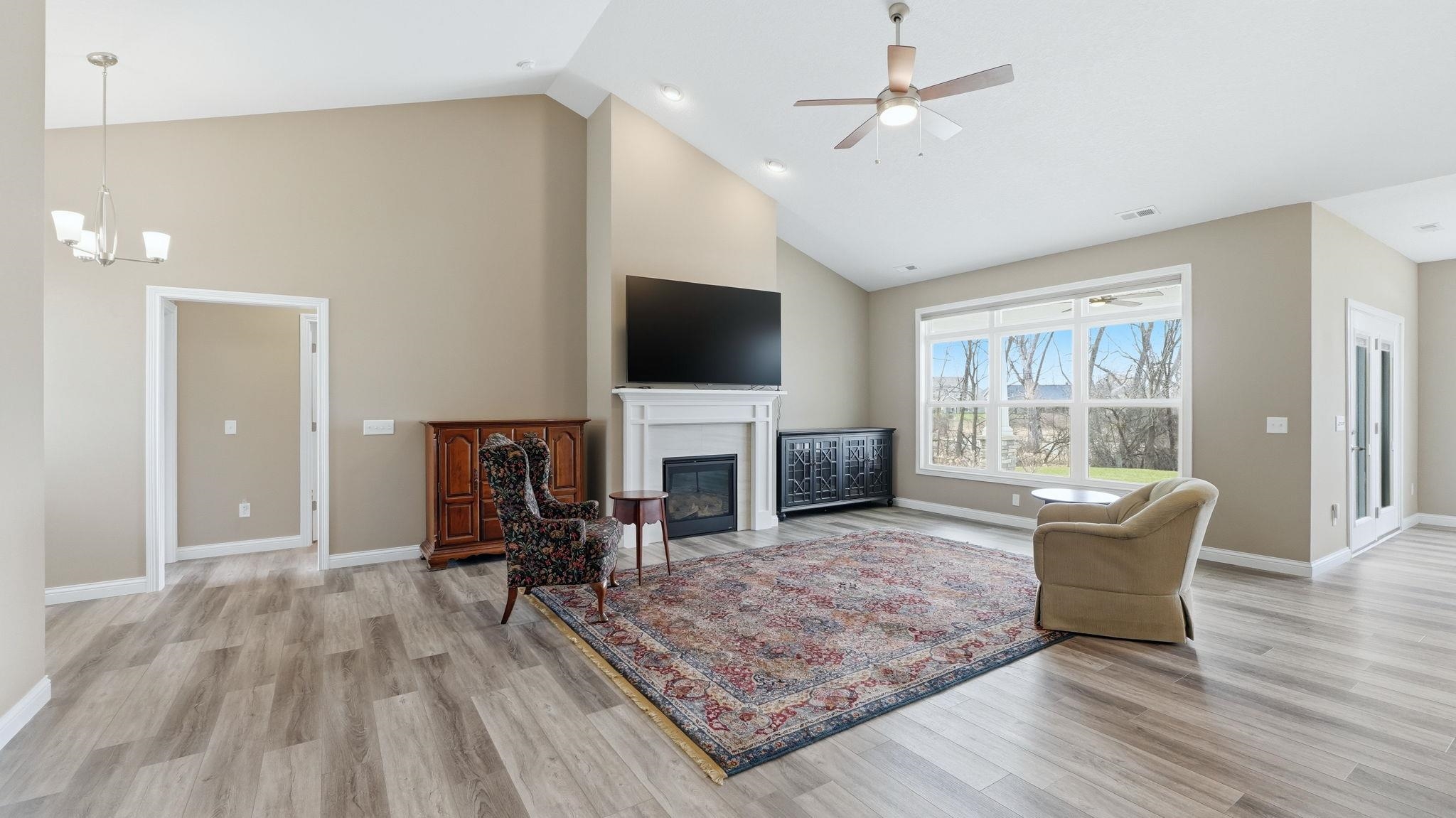 Living area featuring a ceiling fan, light wood-type flooring, lofted ceiling, a fireplace with flush hearth, and suspended lighting