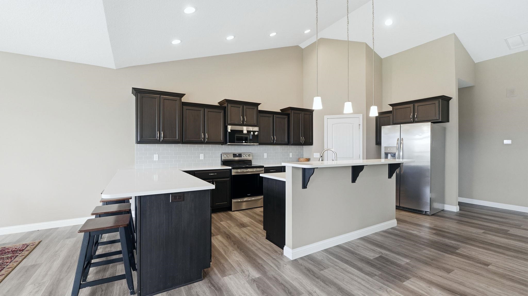 Kitchen with a kitchen breakfast bar, stainless steel appliances, a peninsula, a center island with sink, and vaulted ceiling