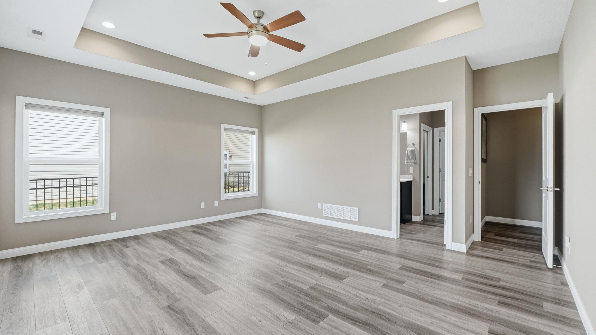 Primary Bedroom with a tray ceiling, ceiling fan, light wood-style flooring, recessed lighting, and connected bathroom
