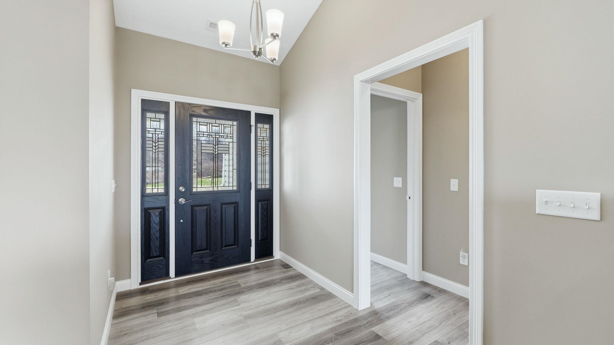 Entryway with light finished floors, hanging lights, and vaulted ceiling