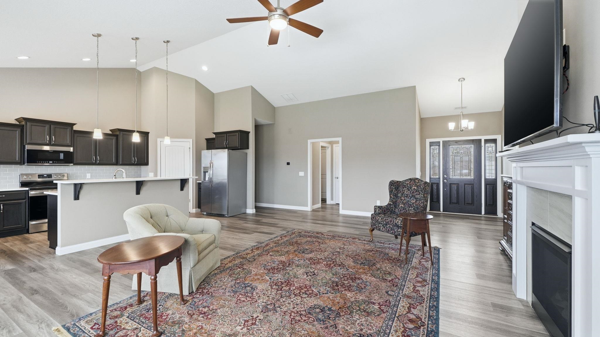 Living area featuring a ceiling fan, a high ceiling, a chandelier, light wood-style flooring, and a fireplace