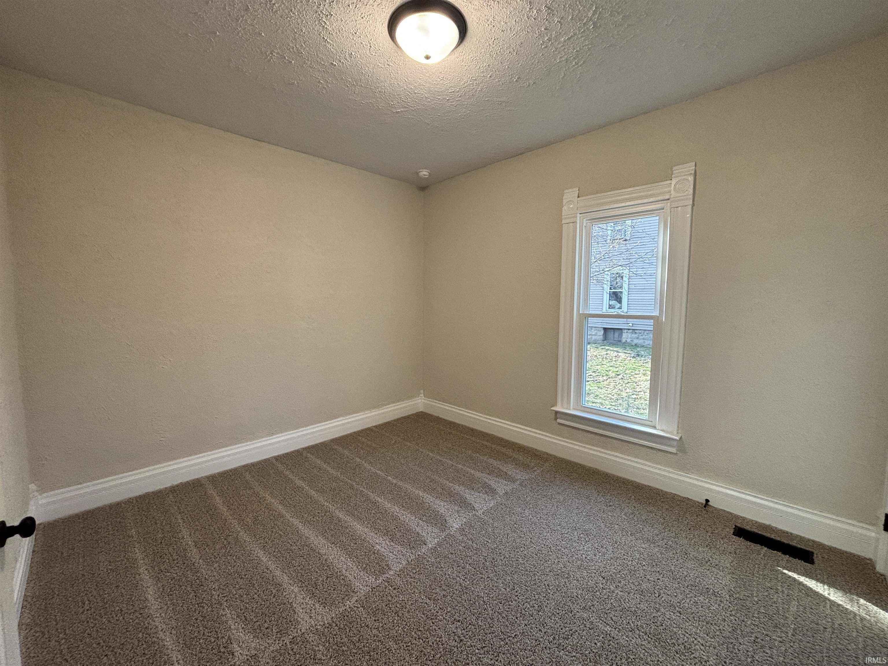 Spare room with dark colored carpet, a textured ceiling, and a textured wall