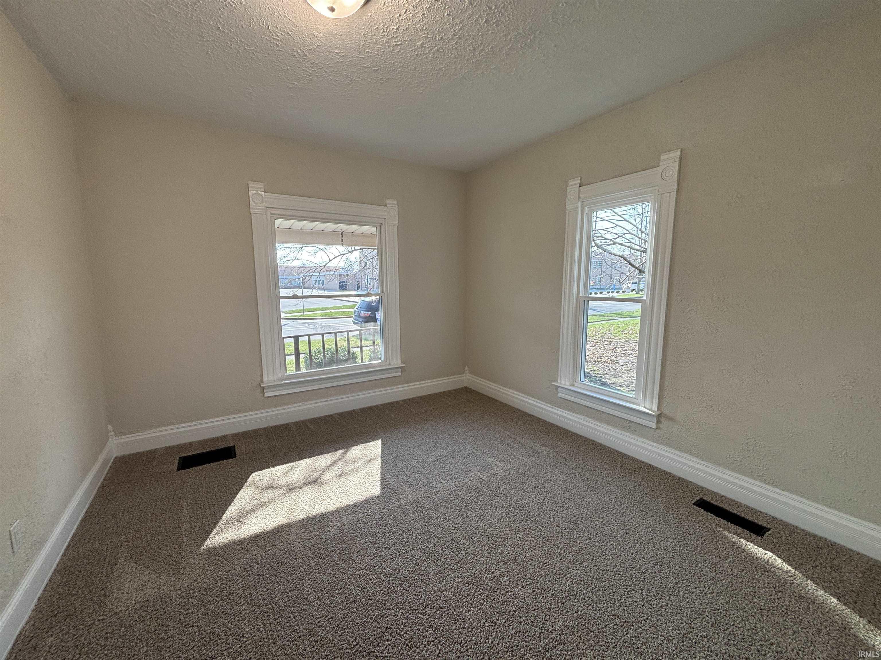Carpeted spare room with healthy amount of natural light, a textured ceiling, and a textured wall