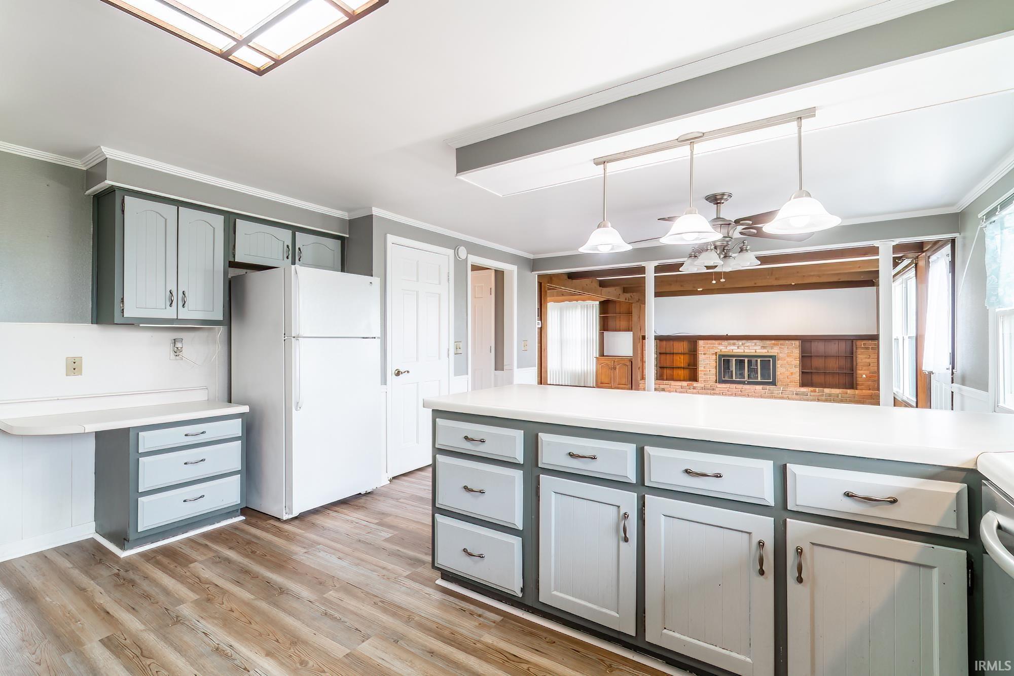 Kitchen with crown molding, light countertops, freestanding refrigerator, ceiling fan, and light wood-style floors
