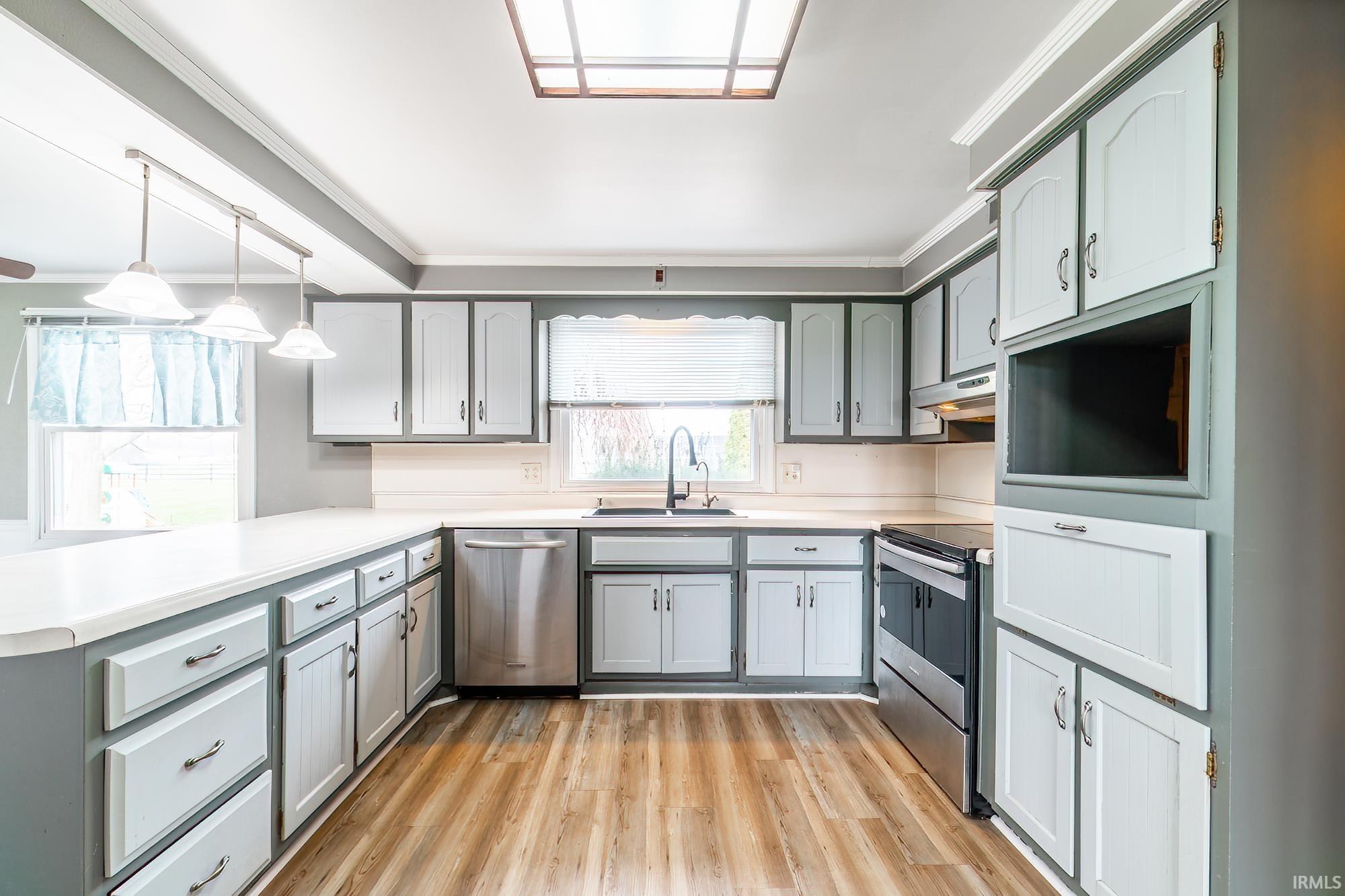 Kitchen featuring gray cabinetry, light countertops, stainless steel appliances, light wood-type flooring, and a peninsula