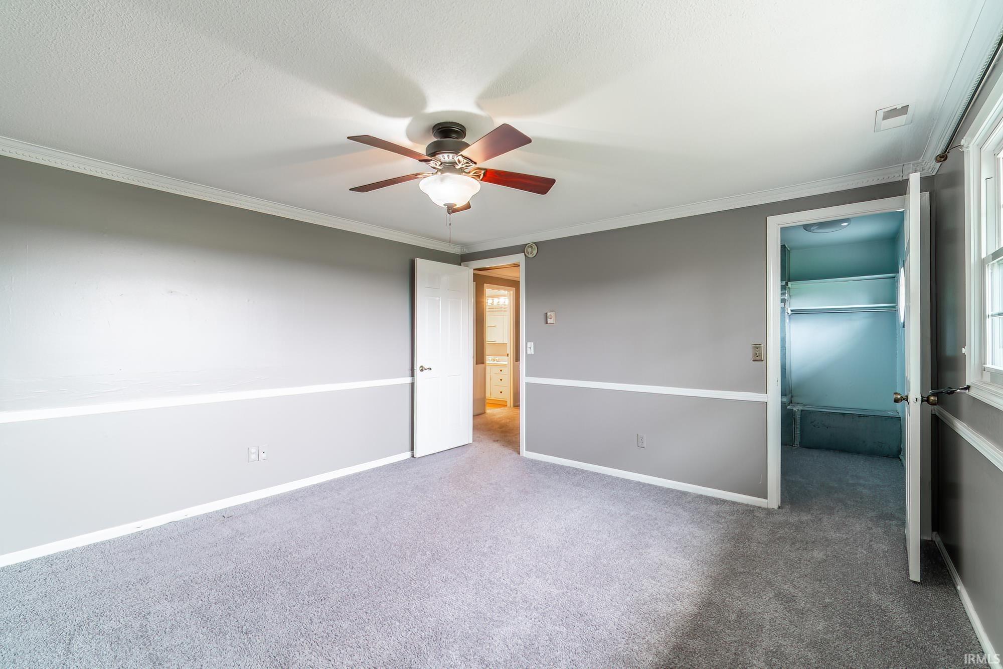Unfurnished bedroom with a walk in closet, crown molding, carpet flooring, and ceiling fan