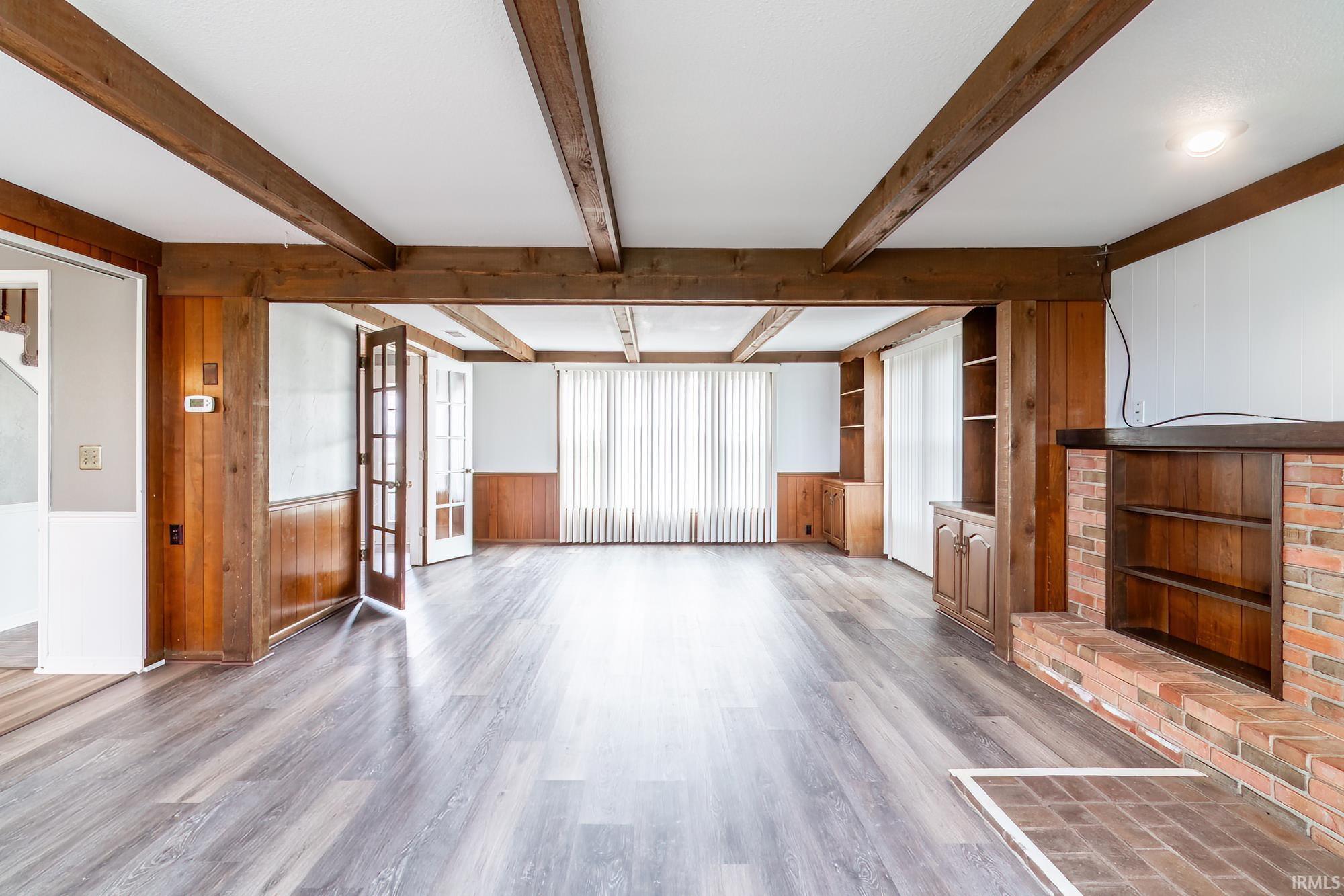 Unfurnished living room with wooden walls, a wainscoted wall, wood finished floors, built in features, and french doors