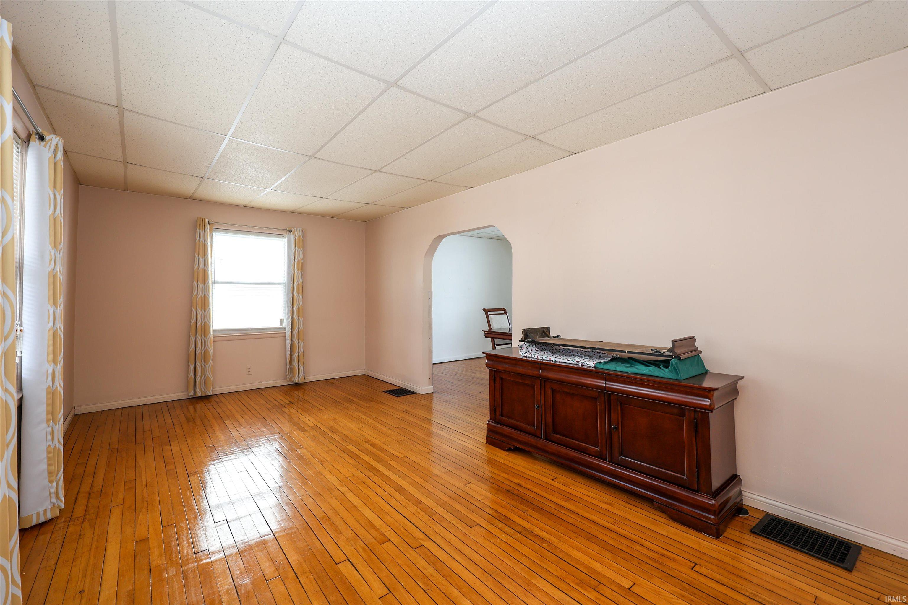 Spare room featuring arched walkways, a paneled ceiling, and light wood finished floors