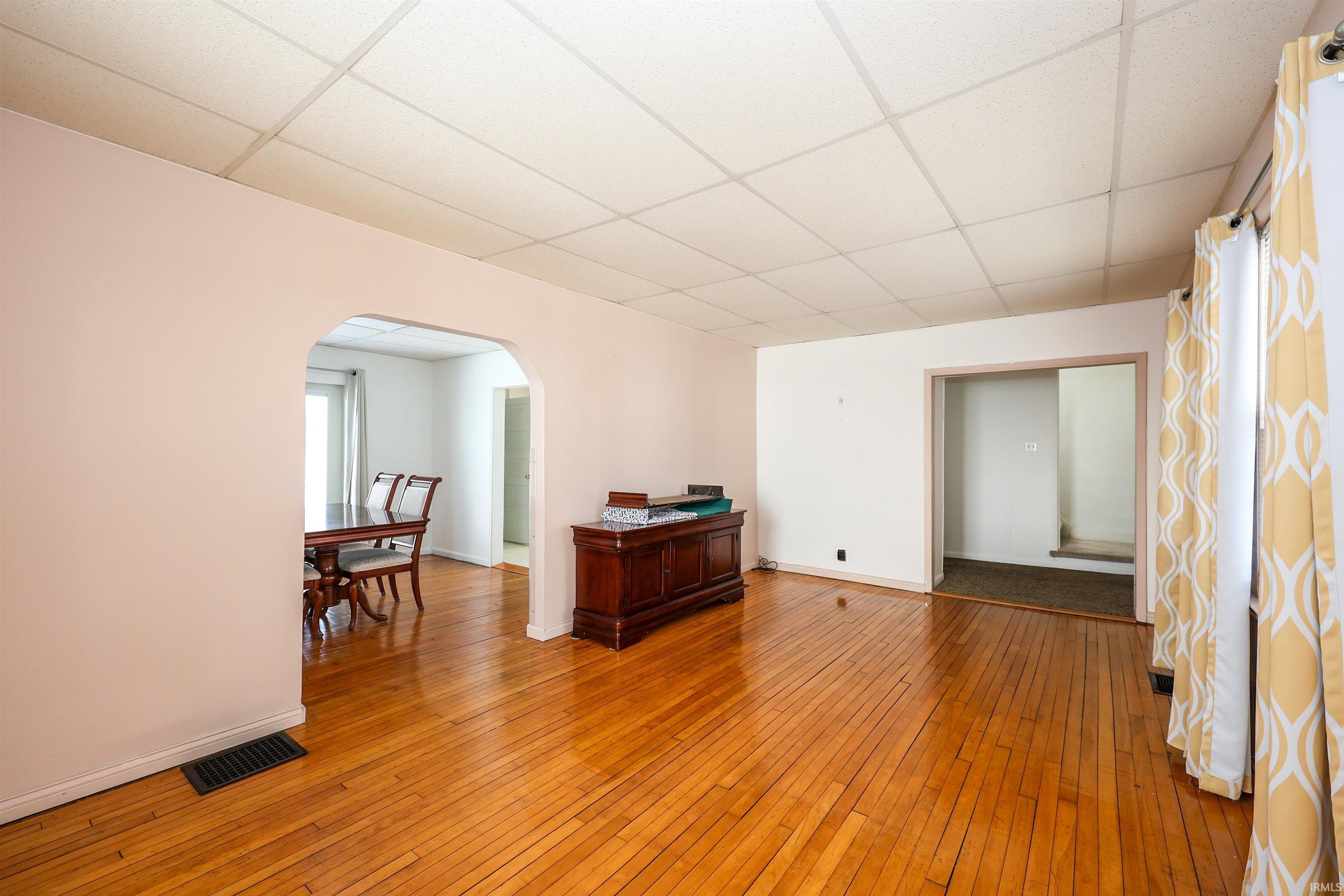 Spare room with light wood-style floors, a drop ceiling, and arched walkways