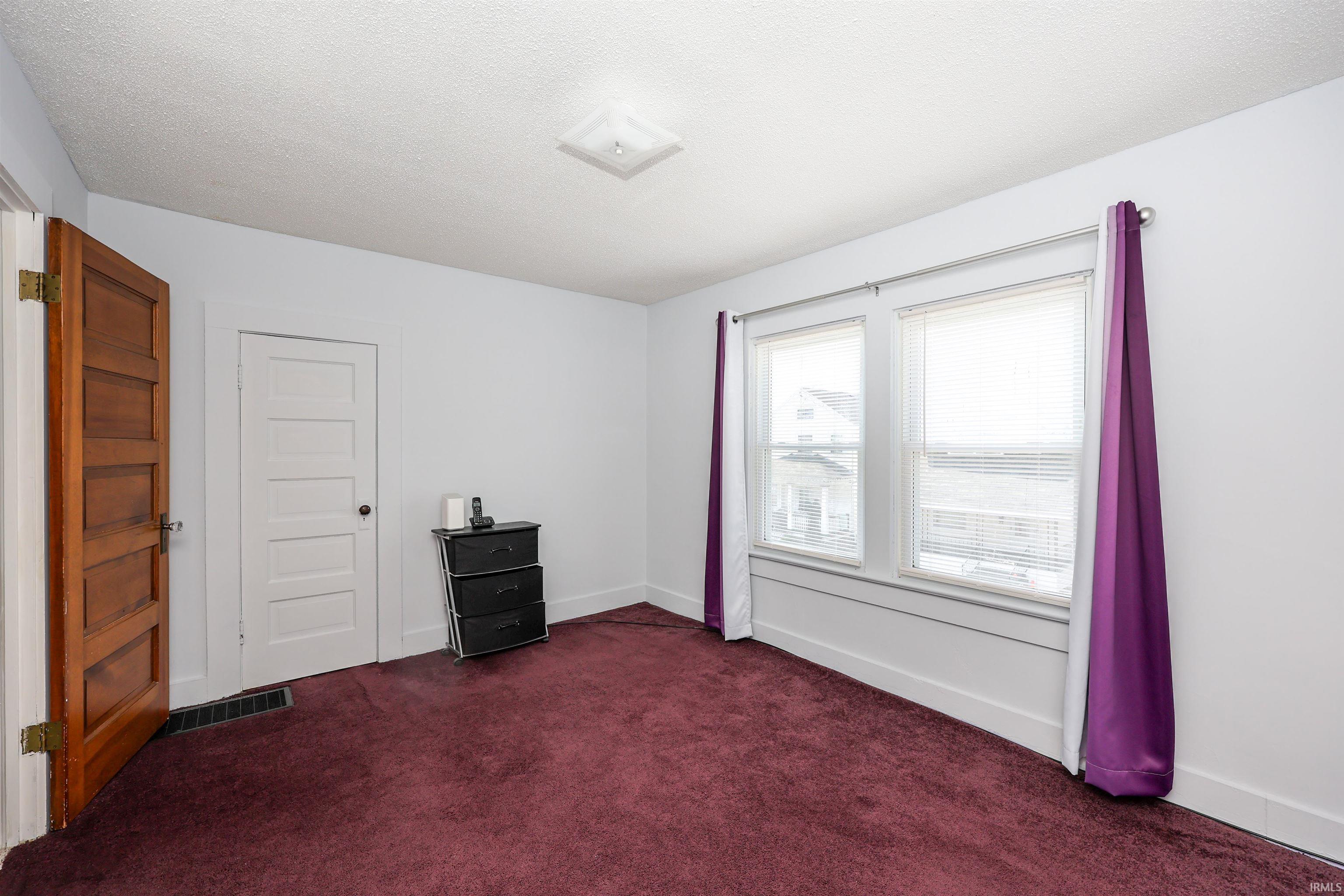 Empty room with dark colored carpet and a textured ceiling