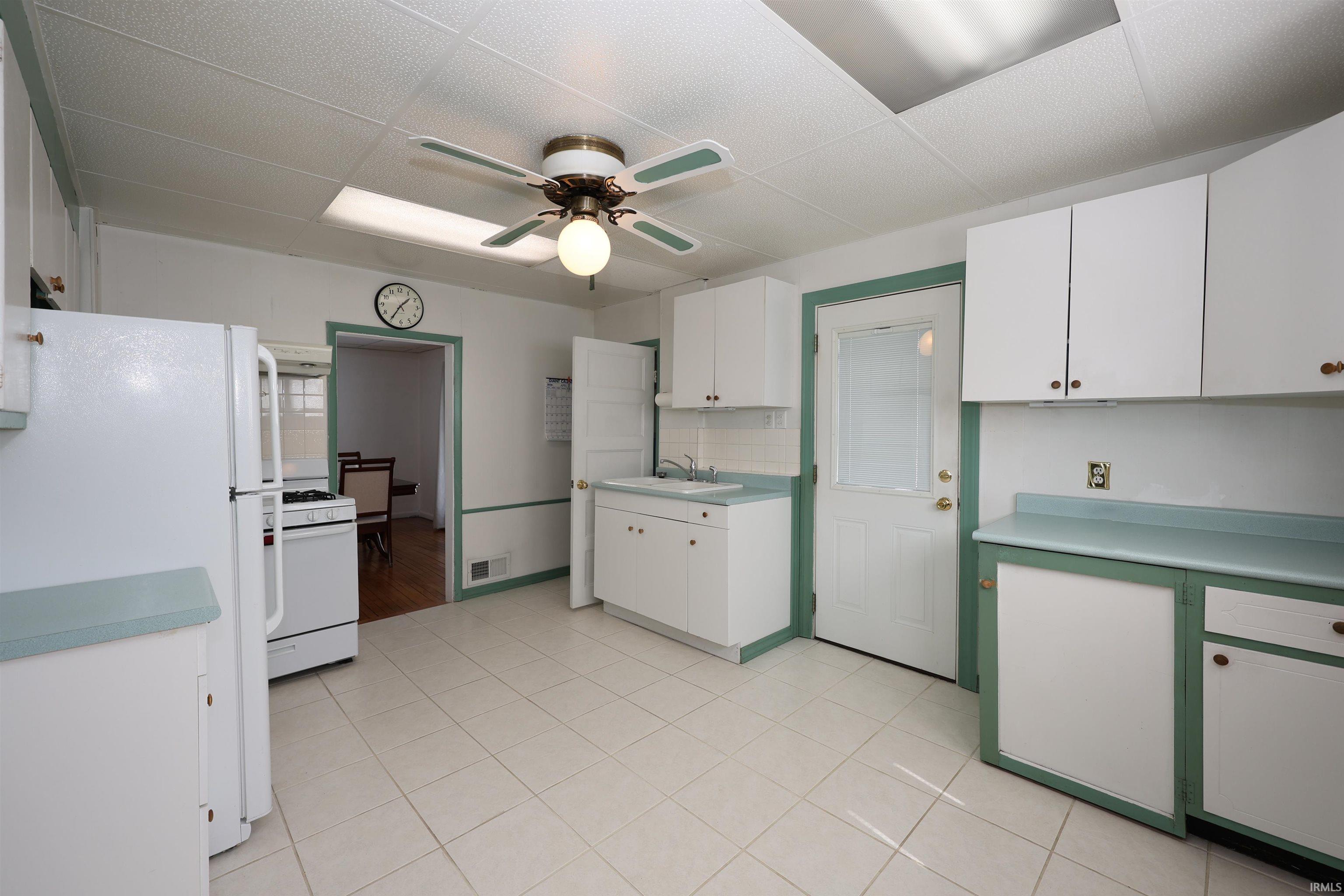 Kitchen featuring white appliances, white cabinets, a ceiling fan, a drop ceiling, and light countertops
