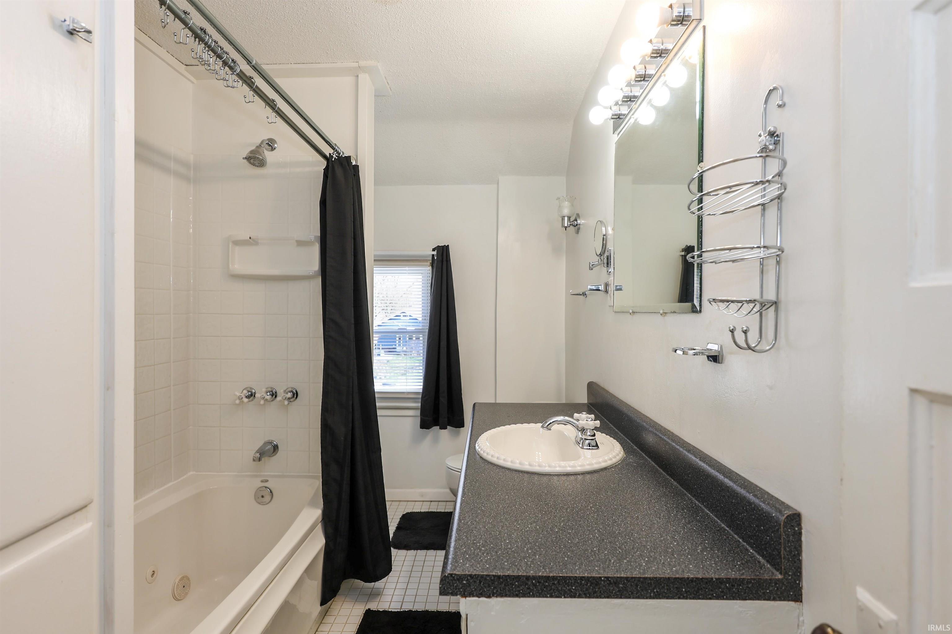 Bathroom featuring a combined bath / shower with jetted tub, vanity, and light tile patterned floors