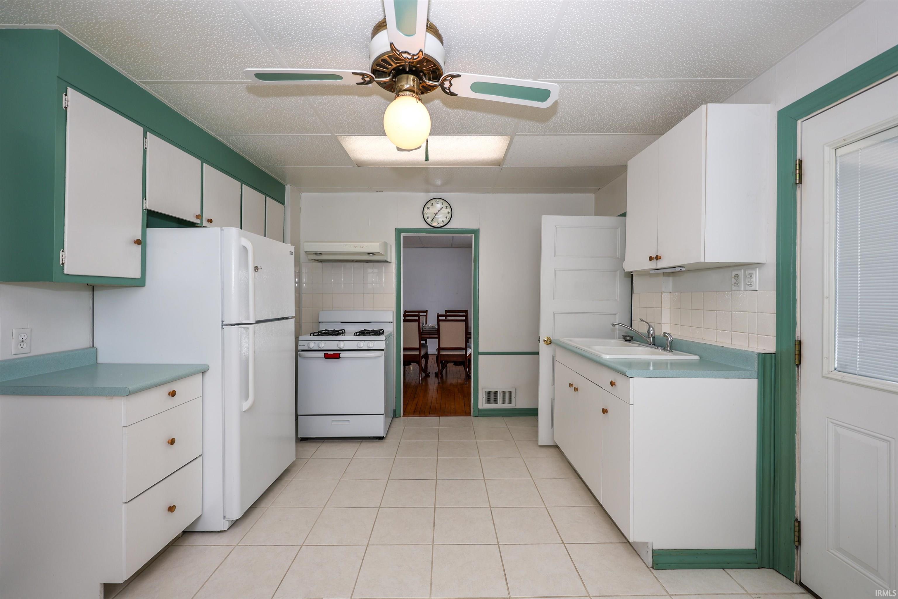Kitchen with white appliances, light countertops, white cabinets, and extractor fan