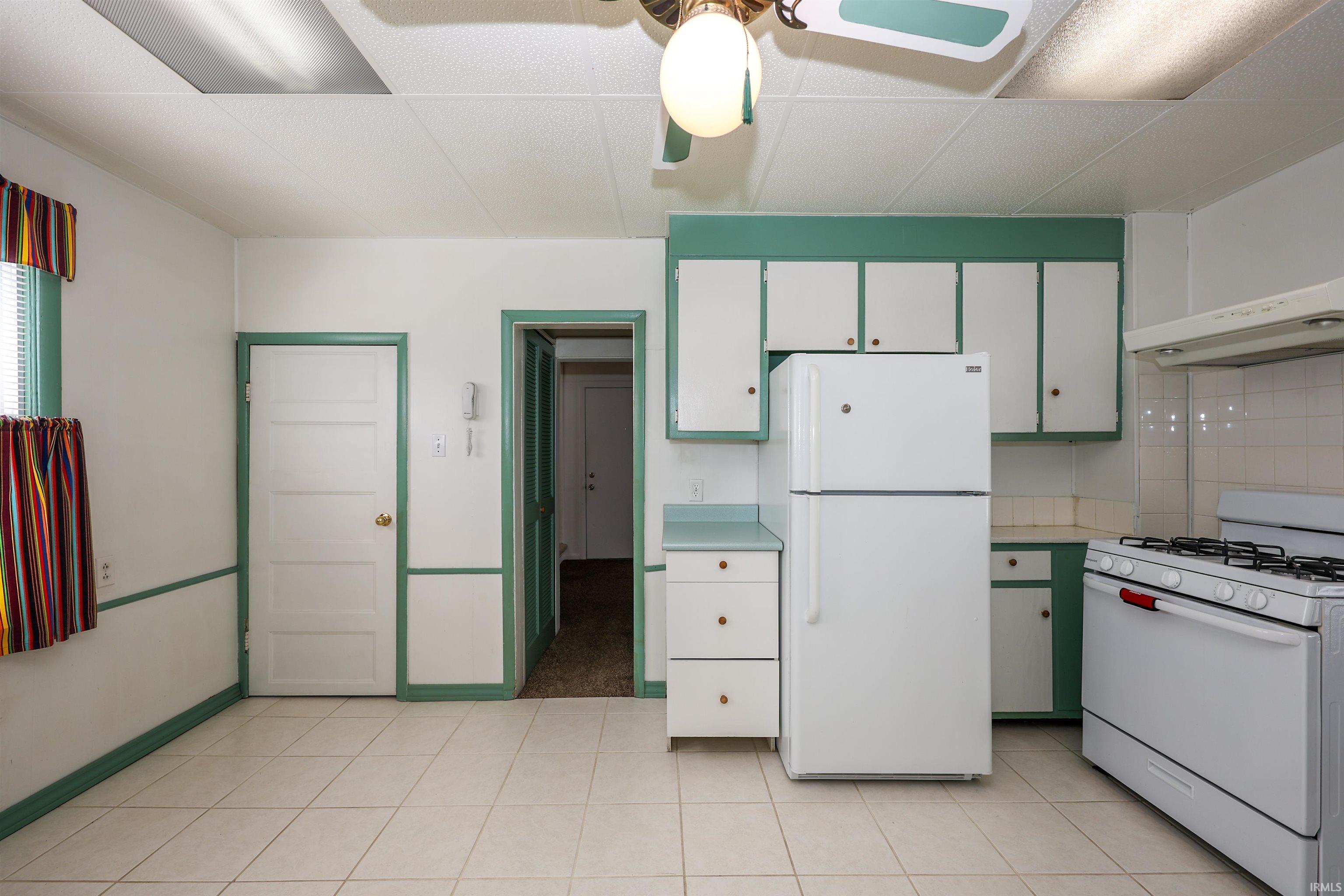 Kitchen featuring white appliances, light countertops, extractor fan, a ceiling fan, and a paneled ceiling