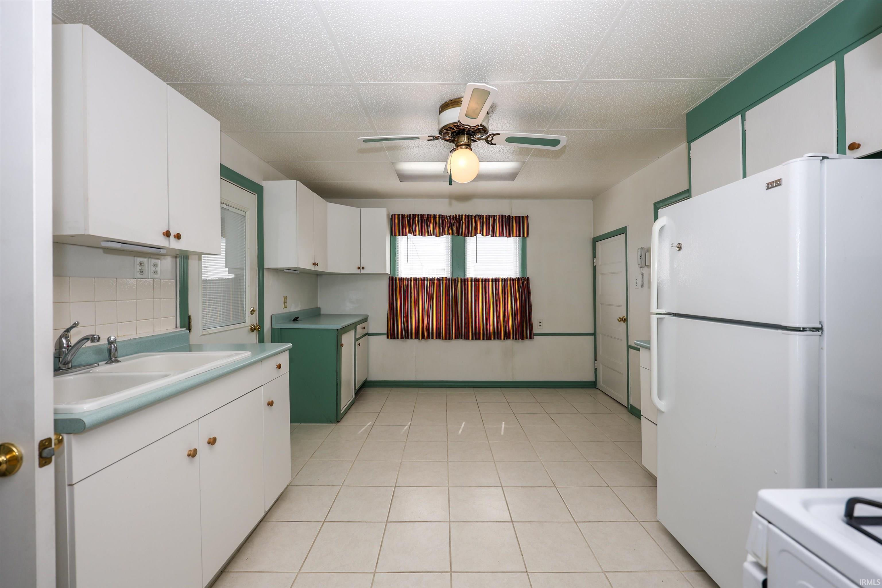 Kitchen featuring white appliances, ceiling fan, two tone color scheme, light countertops, and light tile patterned floors