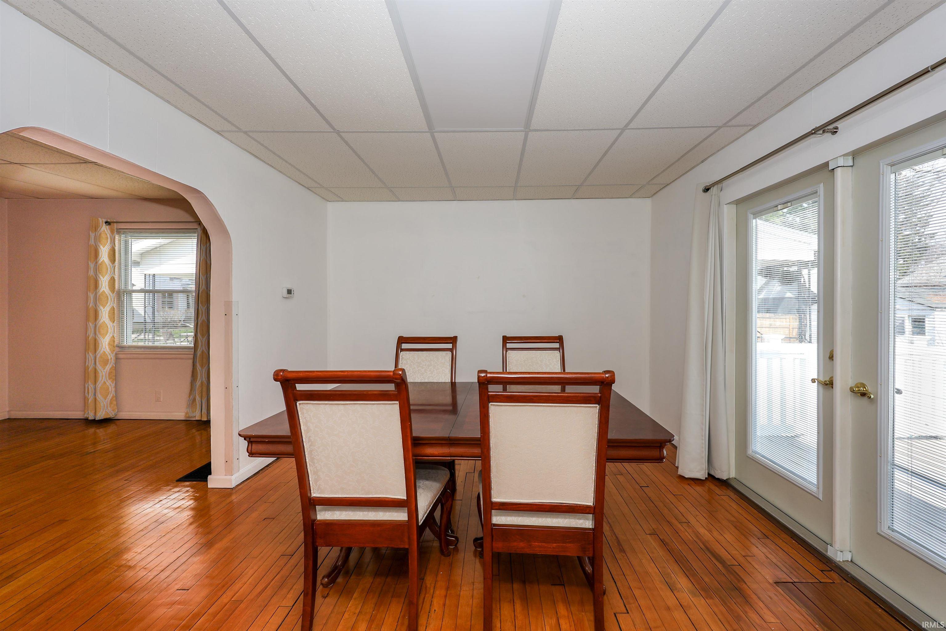 Dining area featuring arched walkways, wood-type flooring, and a drop ceiling