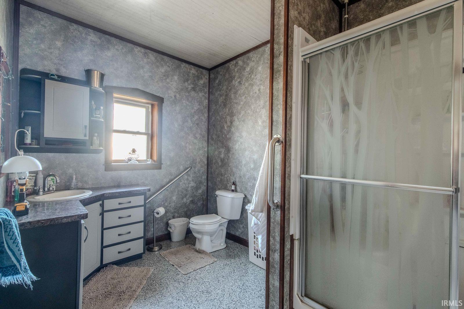 Bathroom with vanity, a stall shower, wallpapered walls, and dark speckled floor