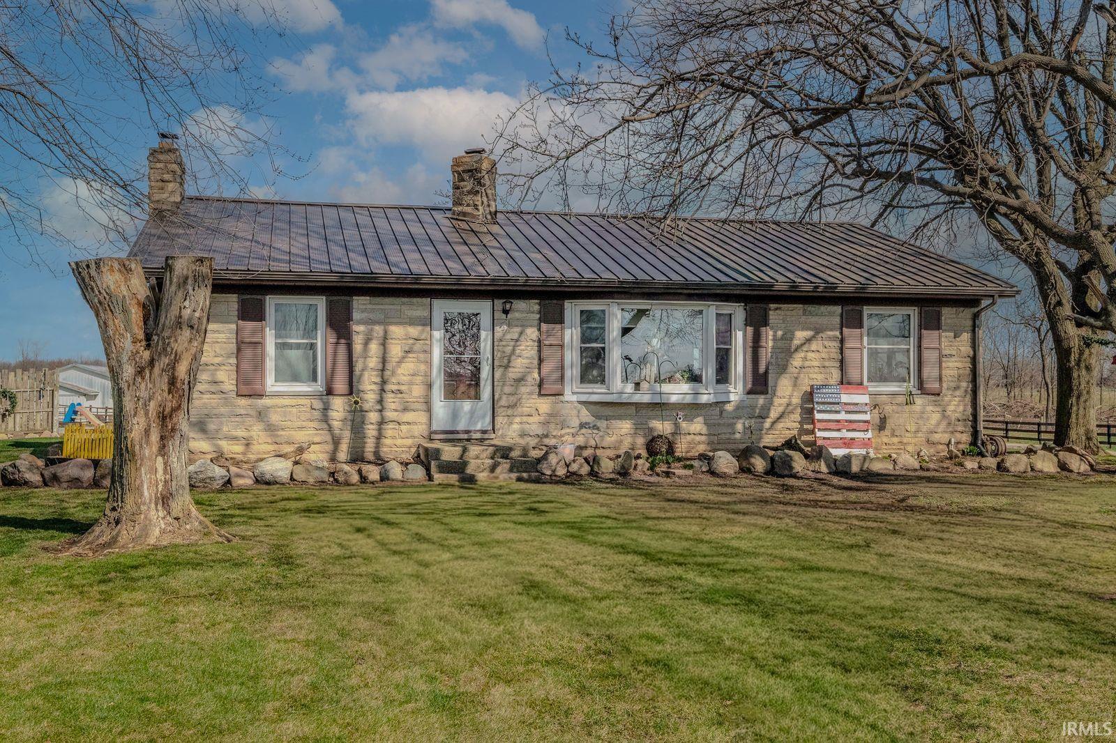 View of front facade featuring a standing seam roof, a chimney, a front yard, and stone siding