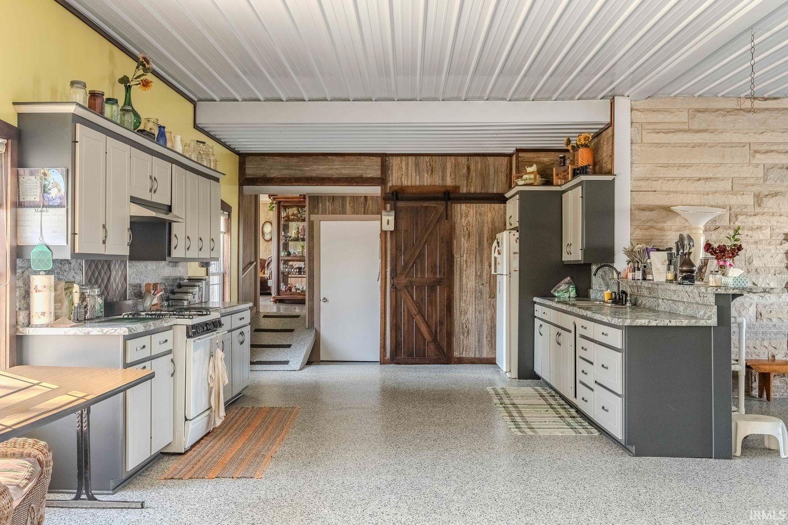 Kitchen with gray cabinetry, a barn door, white appliances, wooden walls, and a peninsula