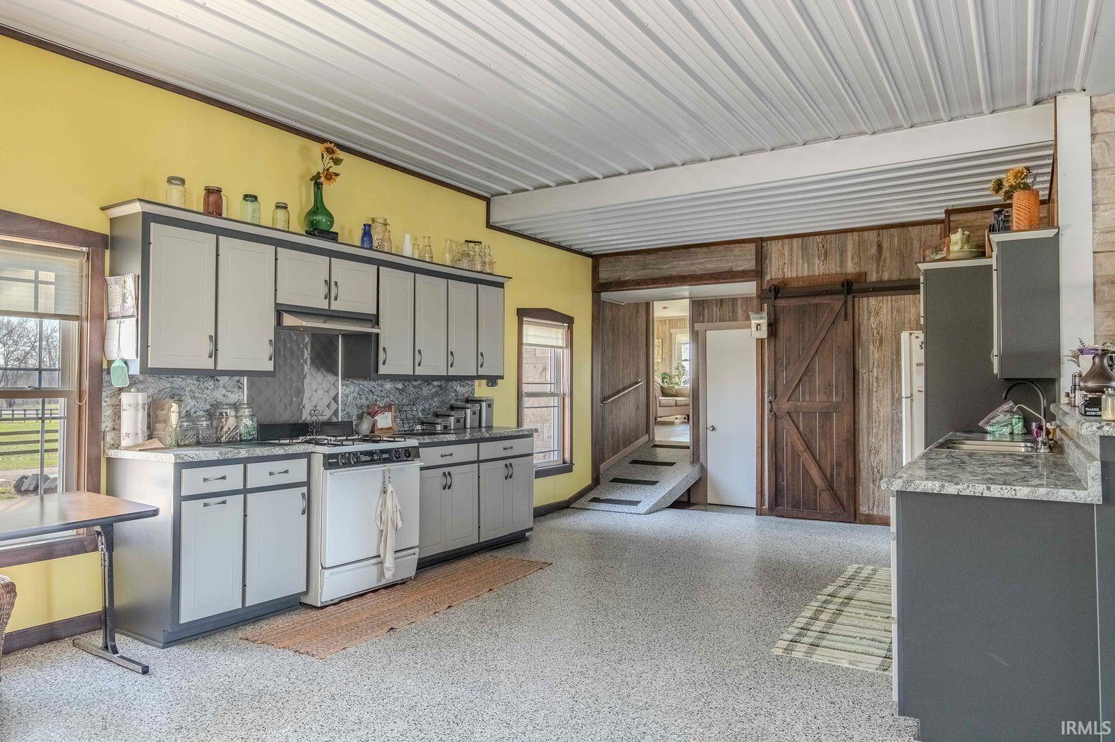 Kitchen with gray cabinetry, a barn door, white gas range, and plenty of natural light
