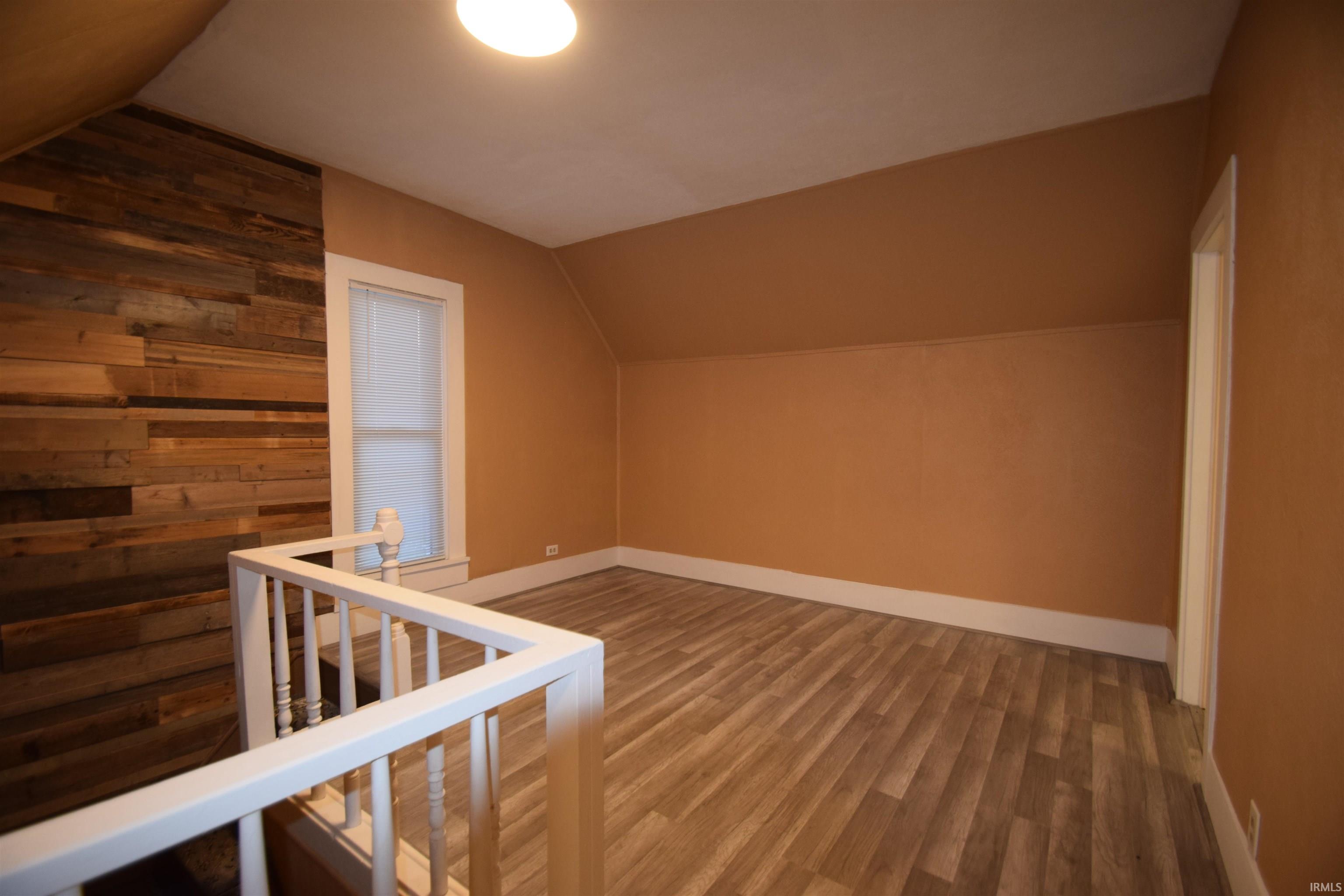 Additional living space with vaulted ceiling, wood finished floors, and wood walls