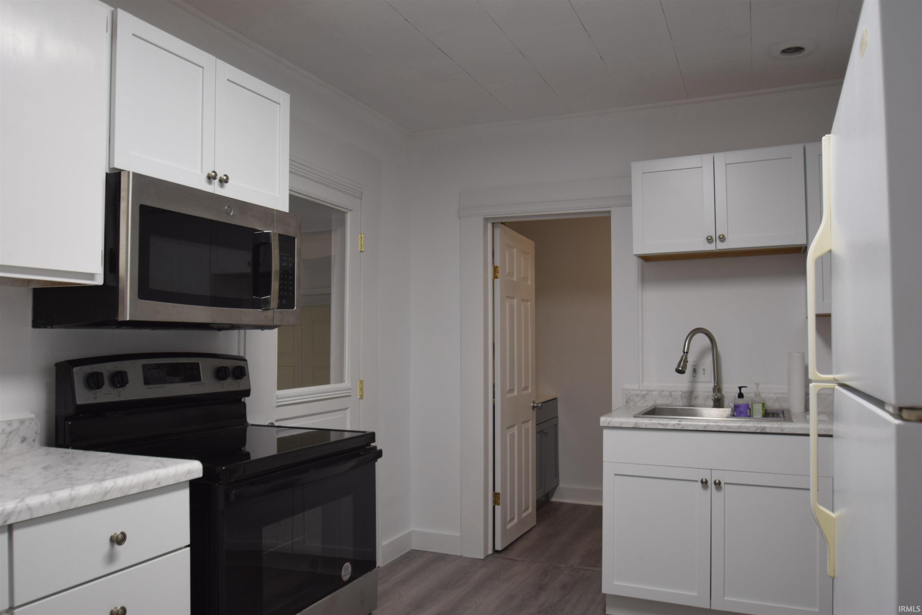 Kitchen featuring stainless steel appliances, light countertops, white cabinets, and dark wood finished floors