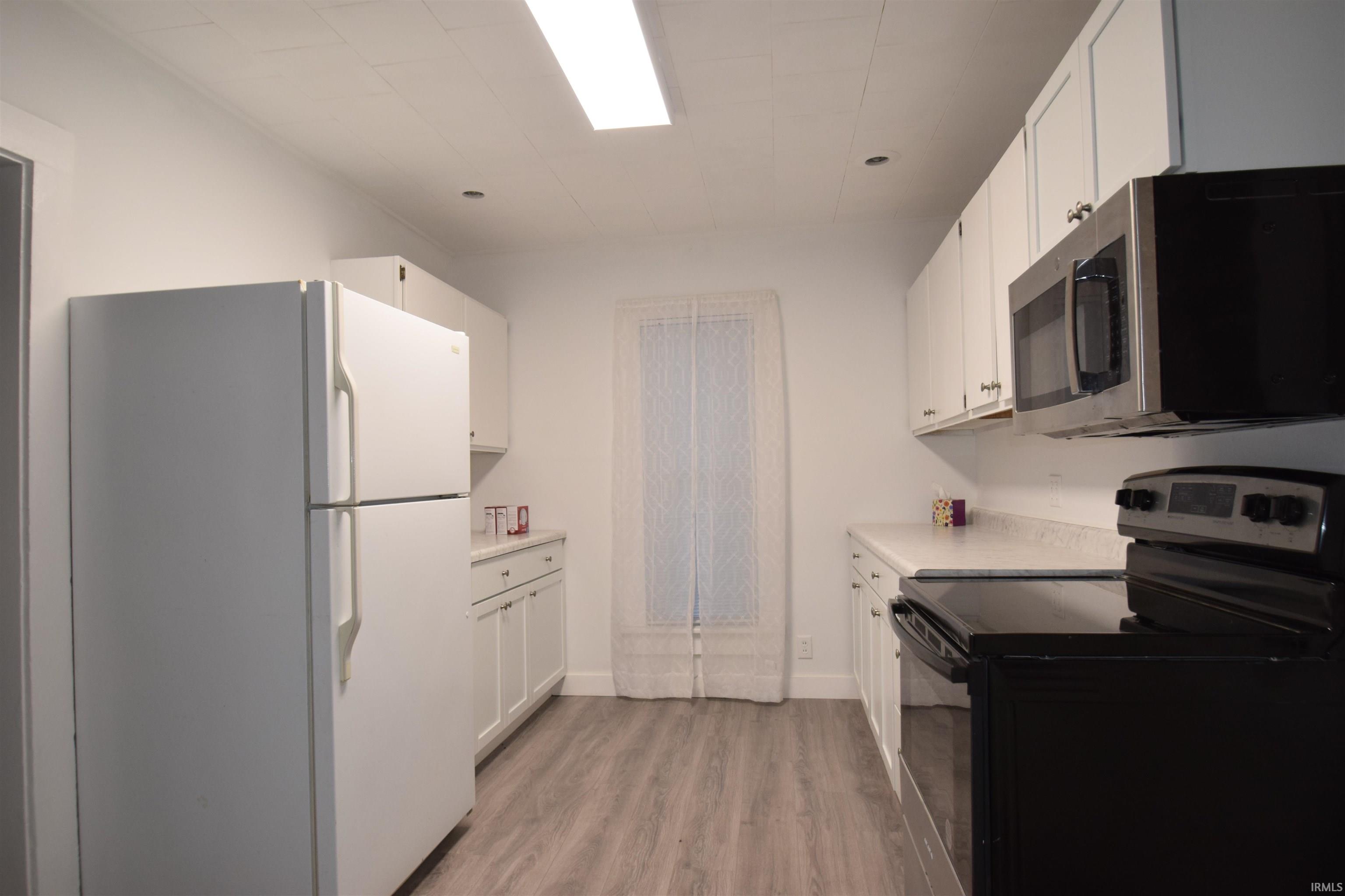 Kitchen featuring black electric range, freestanding refrigerator, light countertops, stainless steel microwave, and white cabinets