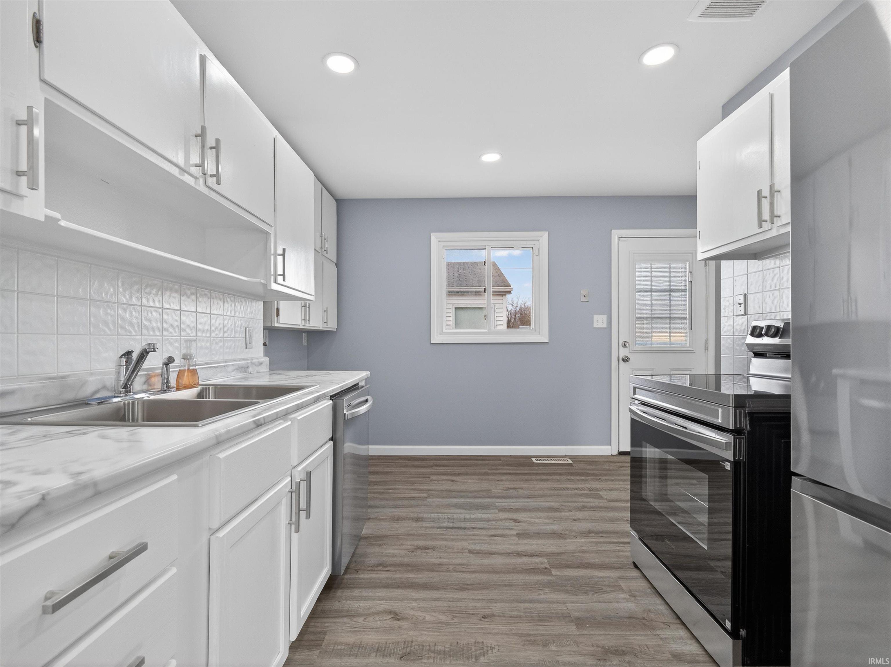 Kitchen featuring white cabinetry, stainless steel appliances, light countertops, tasteful backsplash, and light wood finished floors