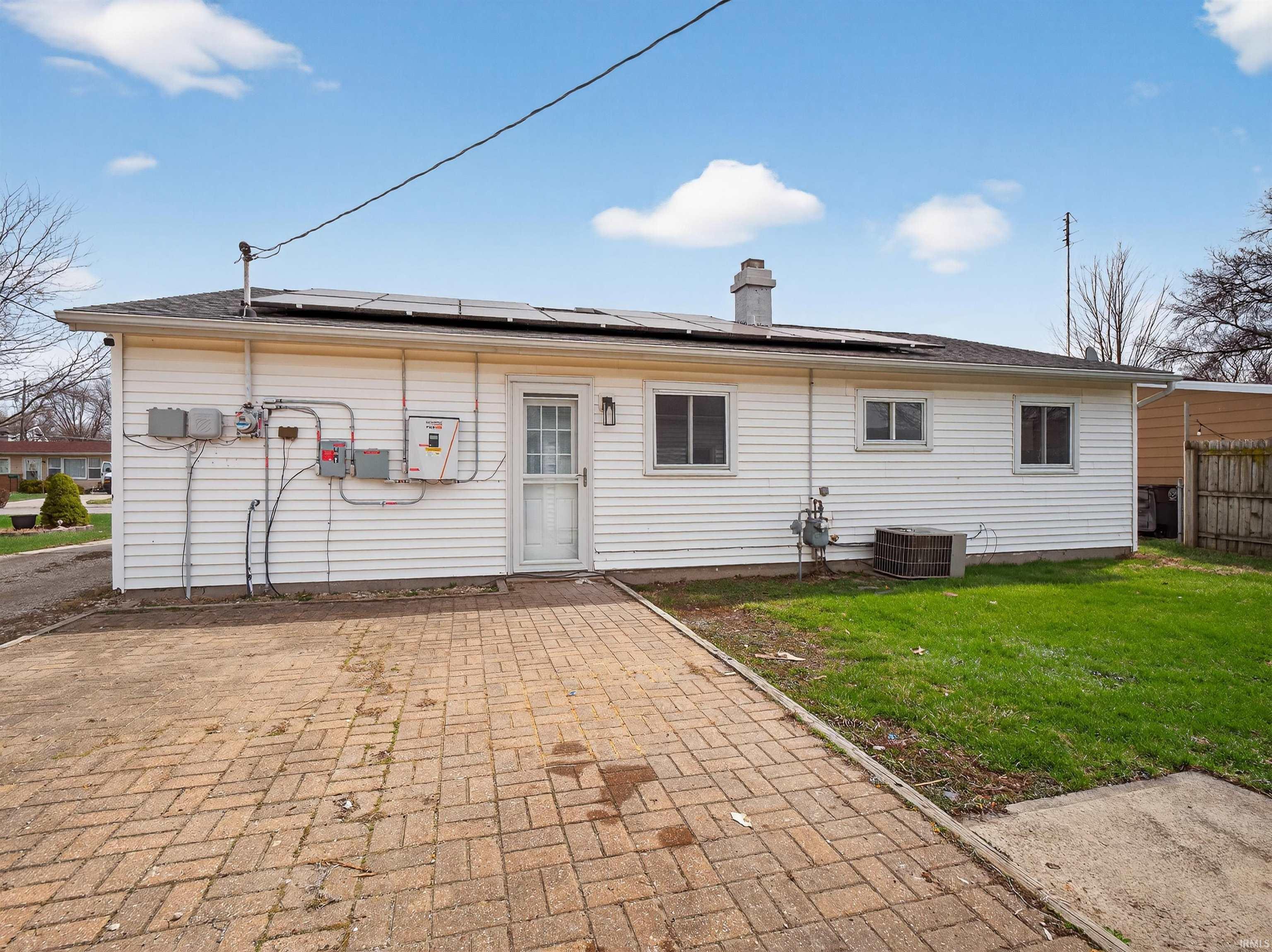 Rear view of property with a patio area, roof mounted solar panels, a yard, and a chimney