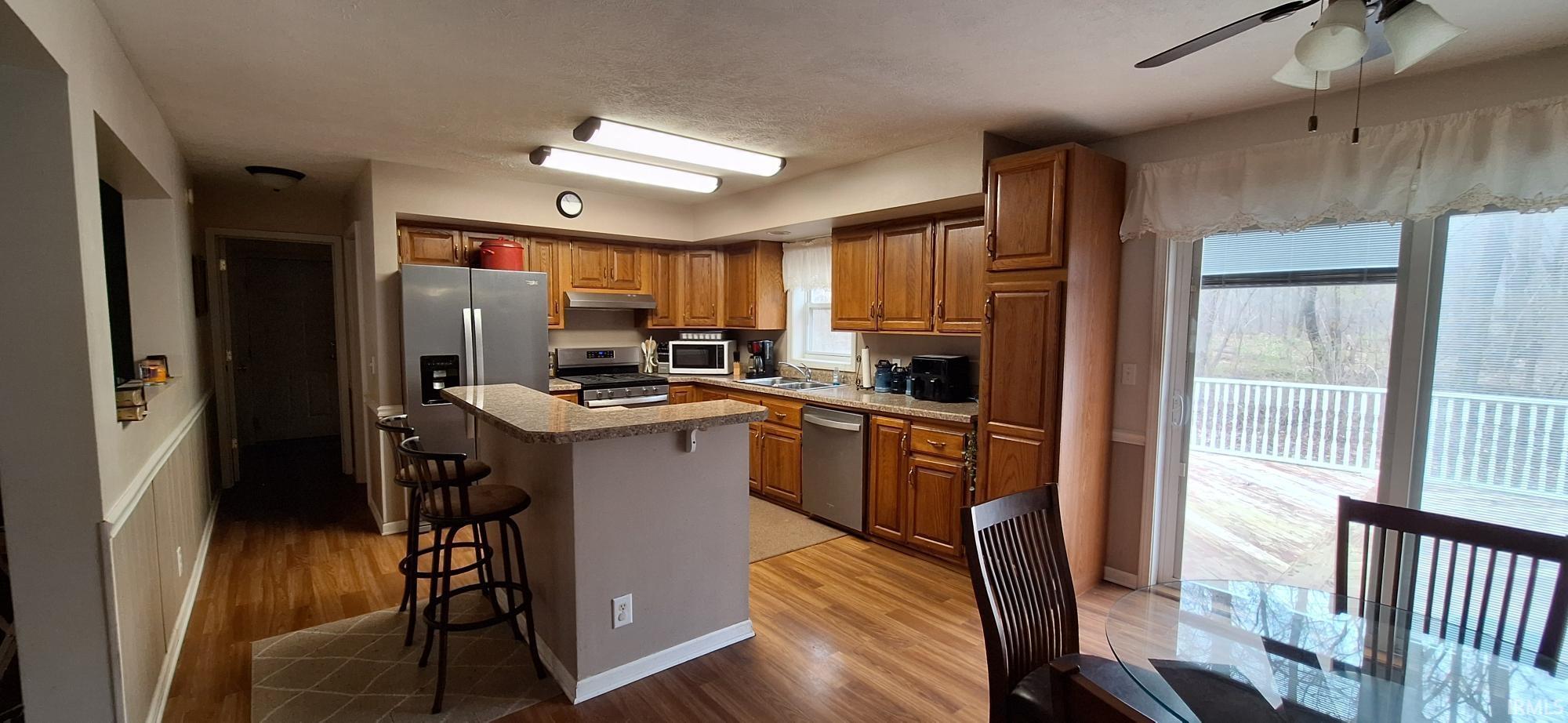 Kitchen featuring wood finish cabinetry, light countertops, stainless steel appliances, a breakfast bar area, and light wood-type flooring